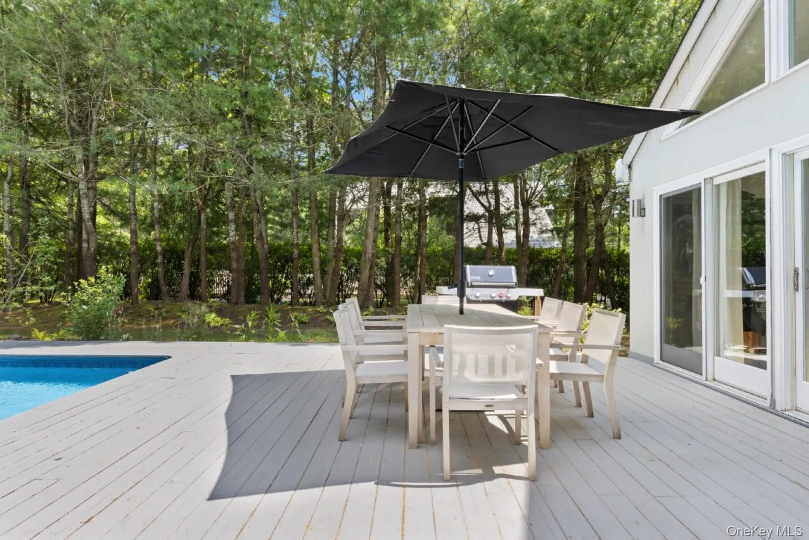 Wooden terrace featuring outdoor dining space, view of wooded area, and a grill Wooden terrace featuring outdoor dining space, view of wooded area, and a grill