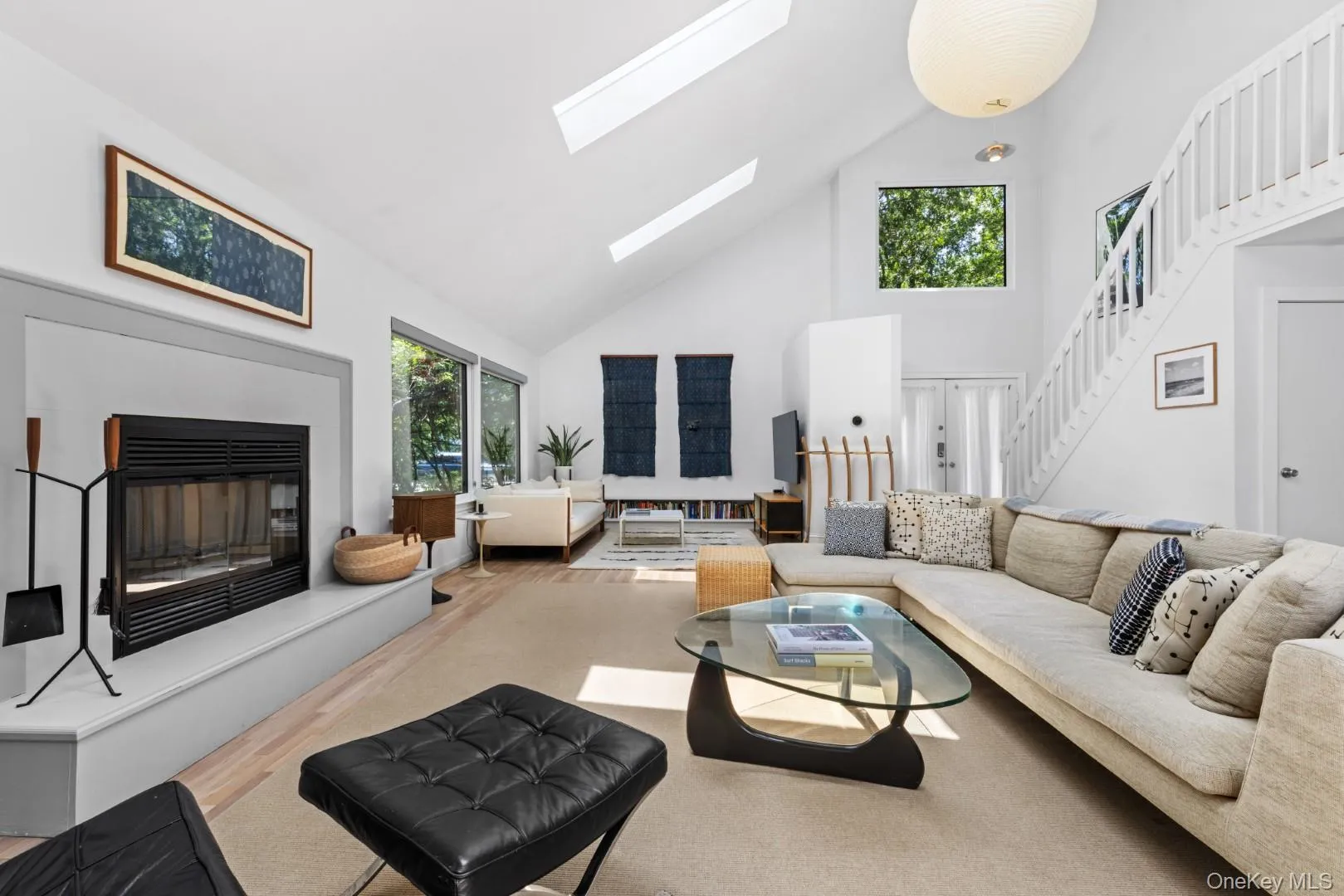 Living room featuring high vaulted ceiling, wood finished floors, a glass covered fireplace, a skylight, and stairs Living room featuring high vaulted ceiling, wood finished floors, a glass covered fireplace, a skylight, and stairs