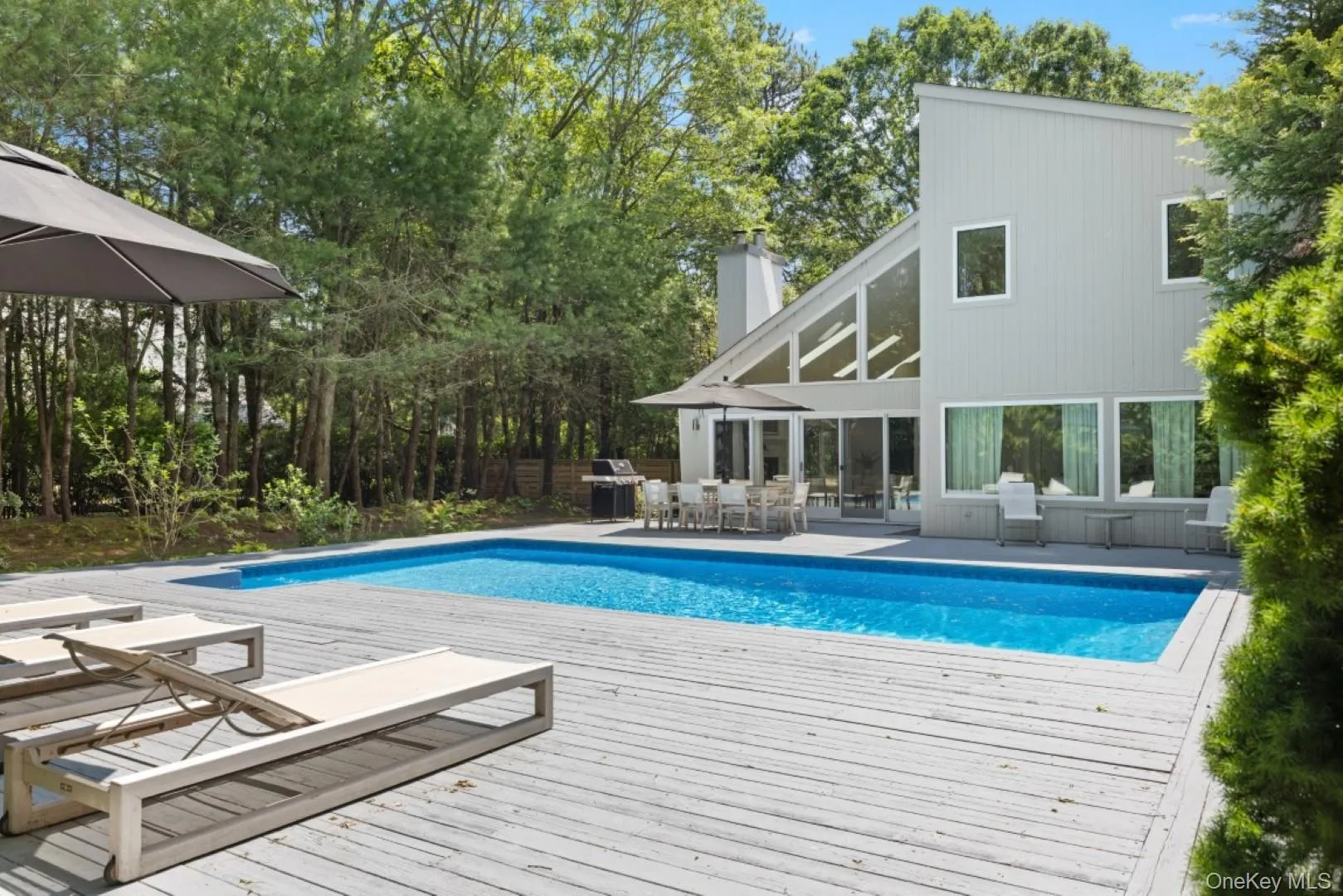 Outdoor pool with a patio, view of scattered trees, area for grilling, and a wooden deck Outdoor pool with a patio, view of scattered trees, area for grilling, and a wooden deck