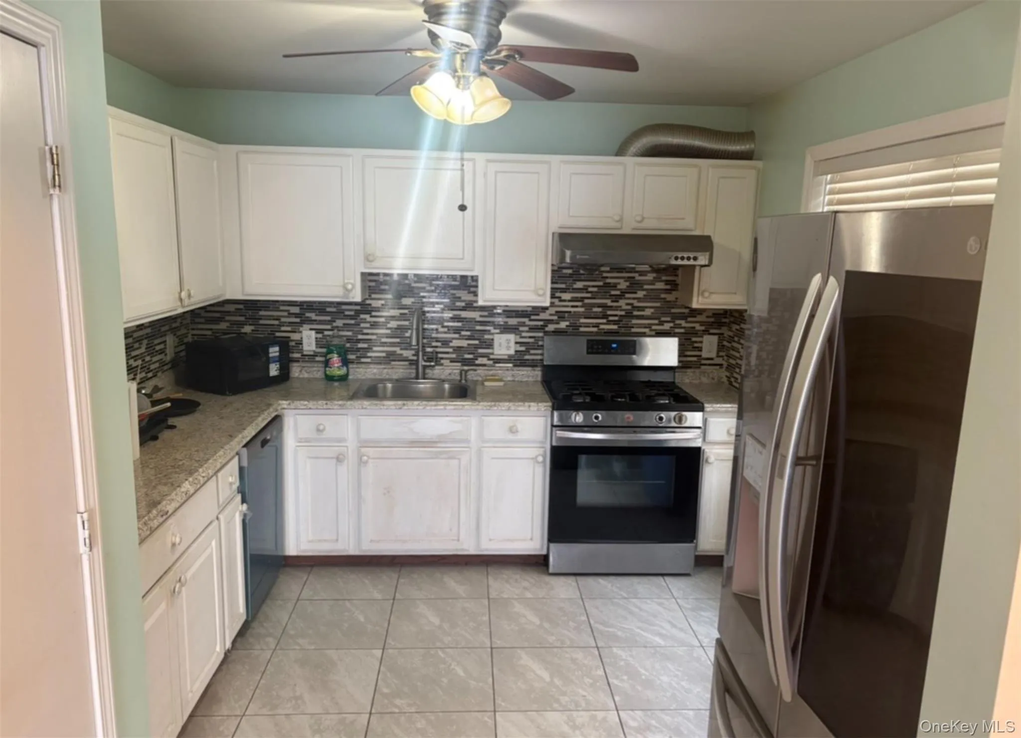 Kitchen featuring appliances with stainless steel finishes, backsplash, under cabinet range hood, and a ceiling fan Kitchen featuring appliances with stainless steel finishes, backsplash, under cabinet range hood, and a ceiling fan