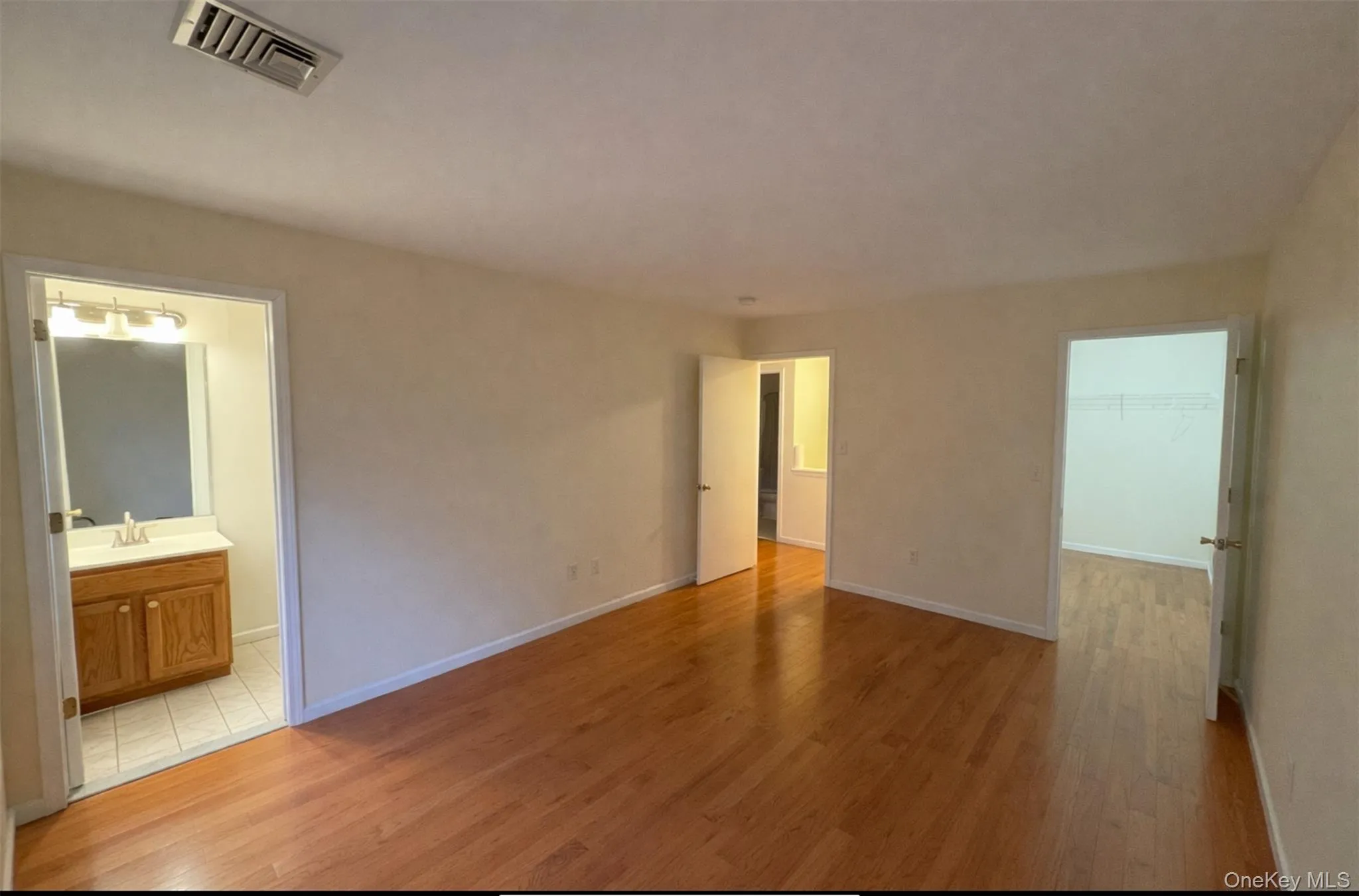 Unfurnished bedroom with light wood finished floors, a walk in closet, and ensuite bath Unfurnished bedroom with light wood finished floors, a walk in closet, and ensuite bath
