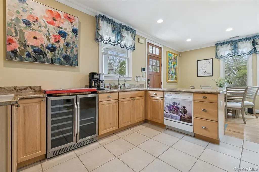 Bar area with light stone counters, beverage cooler, white dishwasher, crown molding, and healthy amount of natural light Bar area with light stone counters, beverage cooler, white dishwasher, crown molding, and healthy amount of natural light