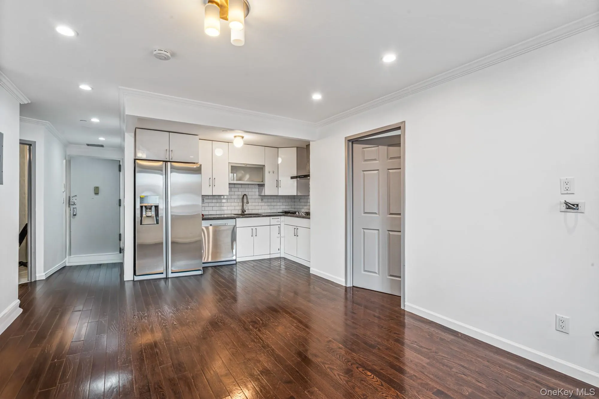 Kitchen with white cabinets, appliances with stainless steel finishes, ornamental molding, recessed lighting, and dark wood-type flooring Kitchen with white cabinets, appliances with stainless steel finishes, ornamental molding, recessed lighting, and dark wood-type flooring