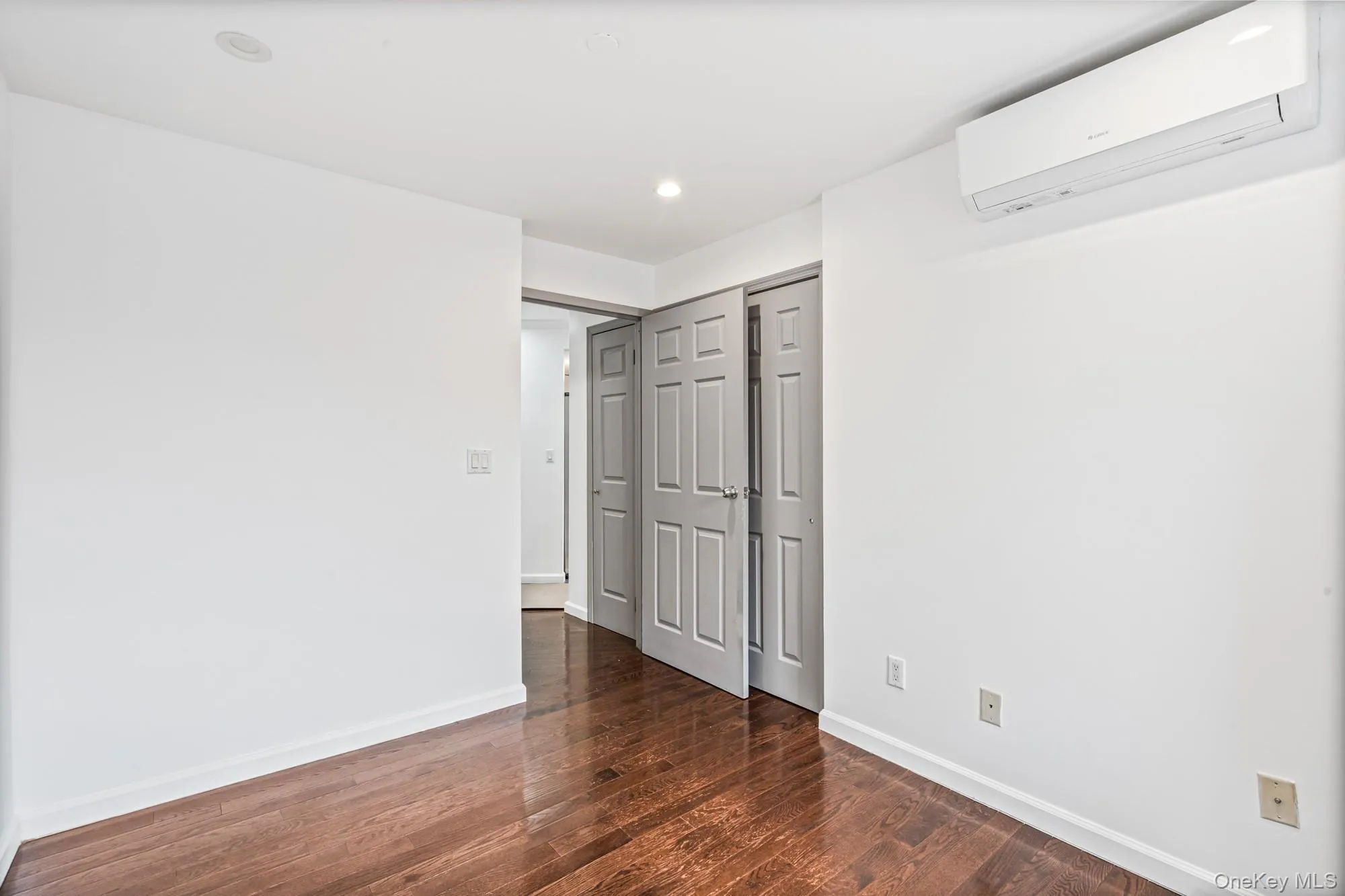 Empty room featuring an AC wall unit, dark wood finished floors, and recessed lighting Empty room featuring an AC wall unit, dark wood finished floors, and recessed lighting