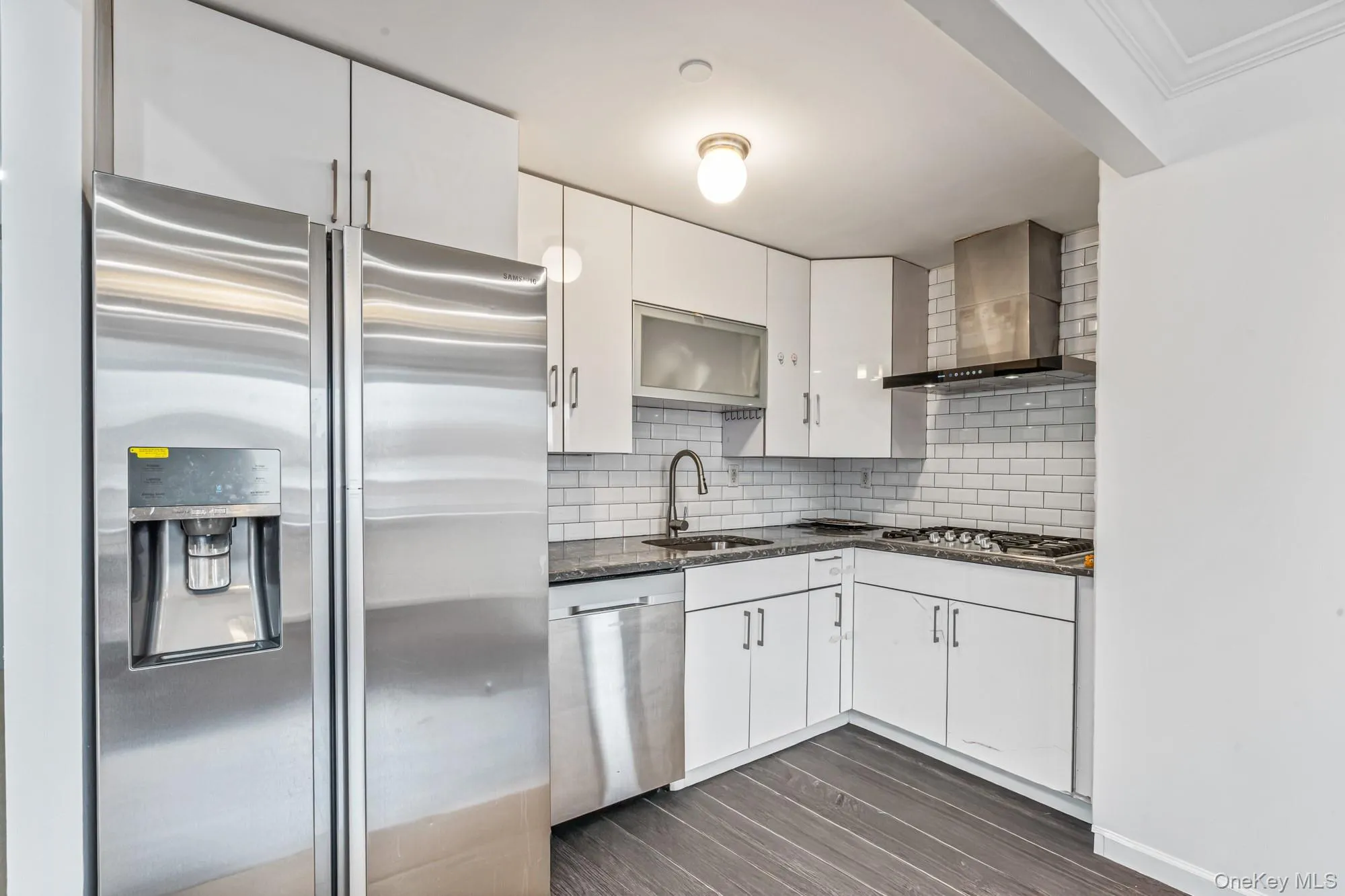 Kitchen featuring appliances with stainless steel finishes, white cabinets, dark stone countertops, wall chimney range hood, and backsplash Kitchen featuring appliances with stainless steel finishes, white cabinets, dark stone countertops, wall chimney range hood, and backsplash
