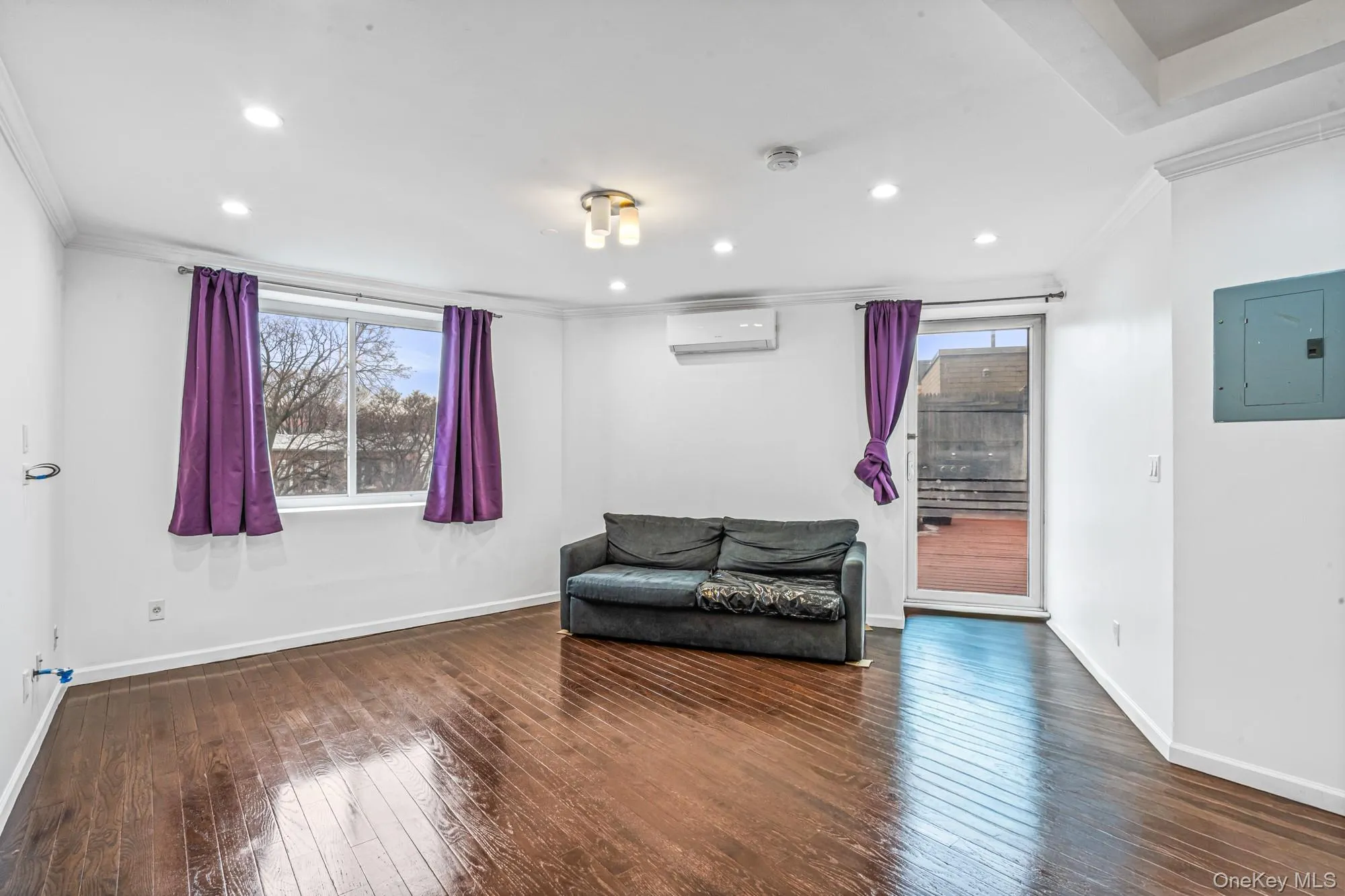 Living area with ornamental molding, electric panel, dark wood-style flooring, recessed lighting, and a wall mounted air conditioner Living area with ornamental molding, electric panel, dark wood-style flooring, recessed lighting, and a wall mounted air conditioner