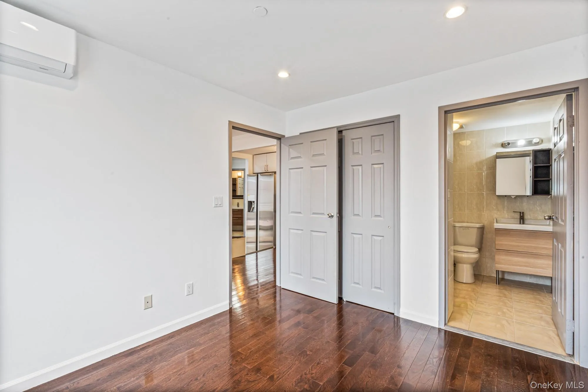 Unfurnished bedroom featuring a wall mounted AC, stainless steel fridge with ice dispenser, dark wood finished floors, connected bathroom, and recessed lighting Unfurnished bedroom featuring a wall mounted AC, stainless steel fridge with ice dispenser, dark wood finished floors, connected bathroom, and recessed lighting