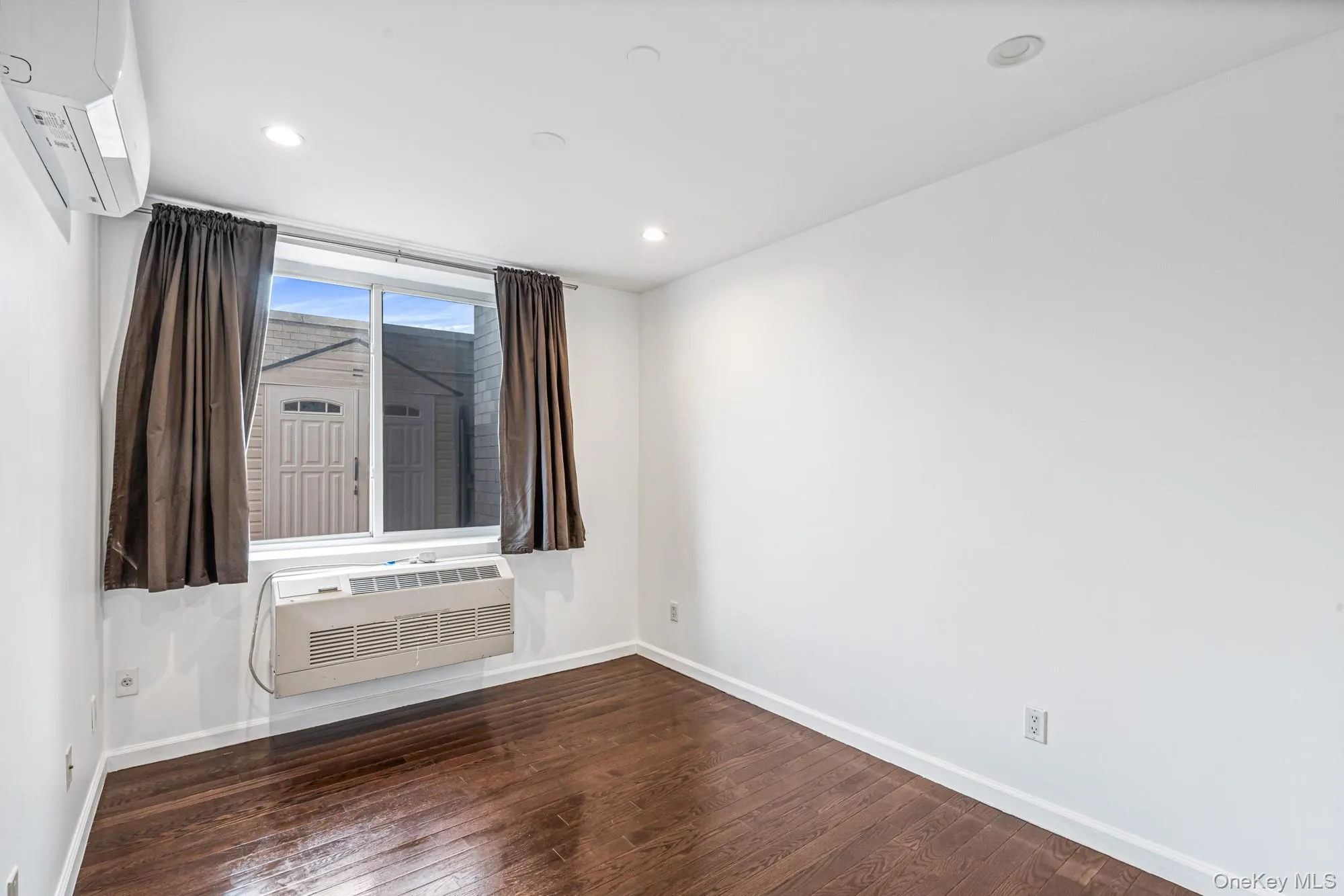 Empty room with dark wood finished floors, an AC wall unit, a wall mounted AC, and recessed lighting Empty room with dark wood finished floors, an AC wall unit, a wall mounted AC, and recessed lighting