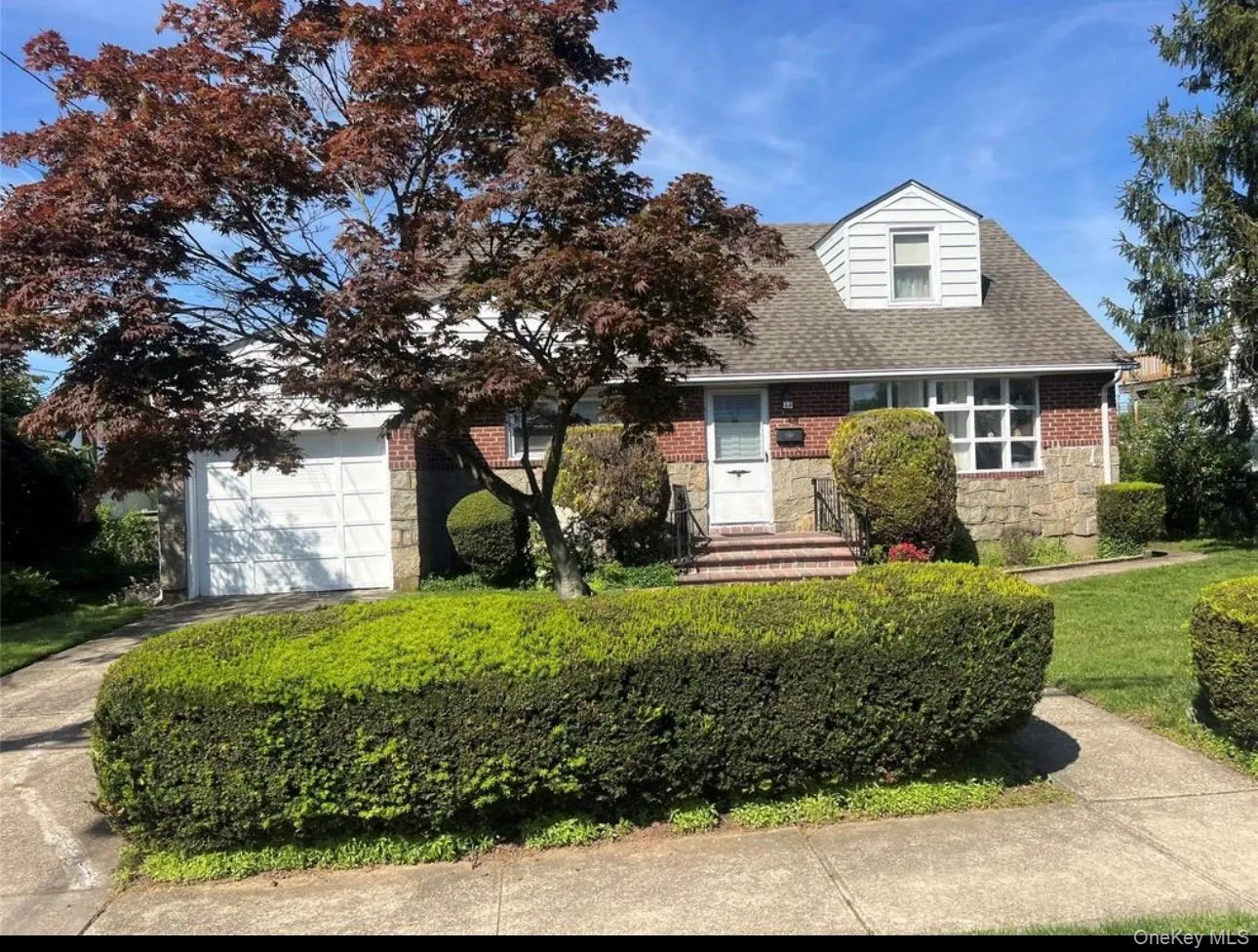 View of front of home with stone siding, a shingled roof, driveway, a front lawn, and brick siding View of front of home with stone siding, a shingled roof, driveway, a front lawn, and brick siding