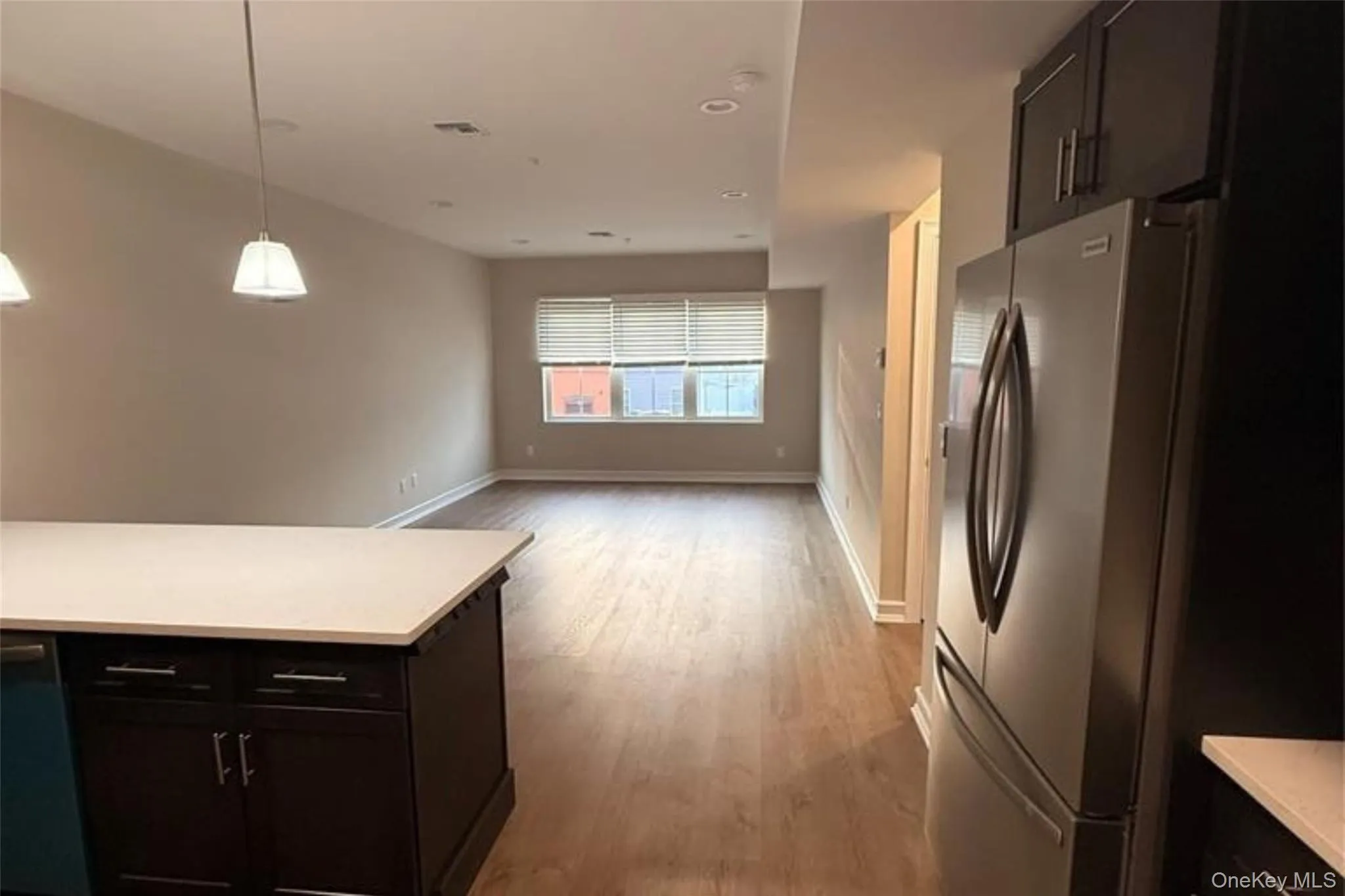 Kitchen featuring dark cabinetry, freestanding refrigerator, hanging light fixtures, and light wood-style flooring Kitchen featuring dark cabinetry, freestanding refrigerator, hanging light fixtures, and light wood-style flooring