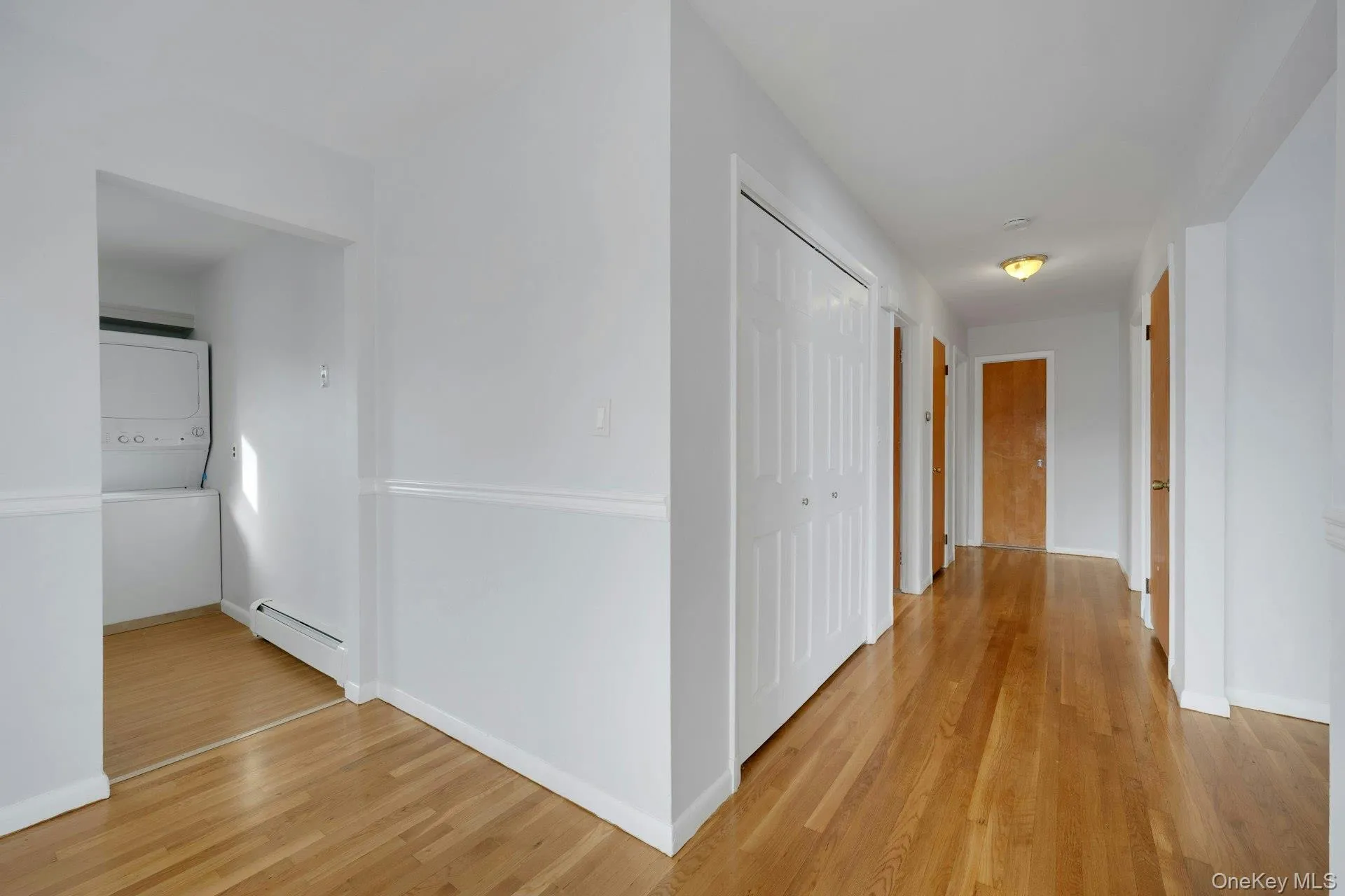 Corridor with light wood-type flooring, baseboard heating, and stacked washing machine and dryer Corridor with light wood-type flooring, baseboard heating, and stacked washing machine and dryer