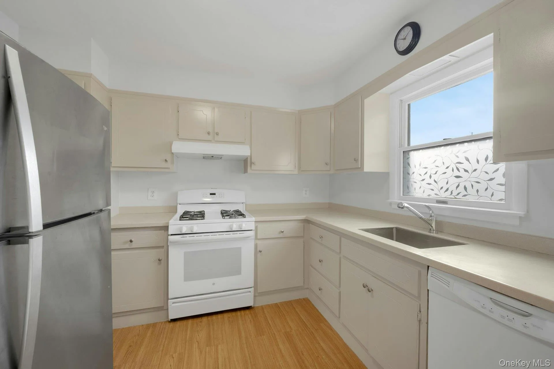 Kitchen with white appliances, light countertops, under cabinet range hood, and light wood-style floors Kitchen with white appliances, light countertops, under cabinet range hood, and light wood-style floors