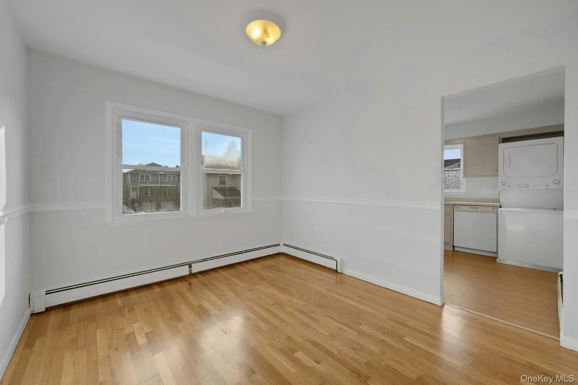 Empty room with a baseboard radiator, stacked washer and clothes dryer, and light wood-style flooring Empty room with a baseboard radiator, stacked washer and clothes dryer, and light wood-style flooring