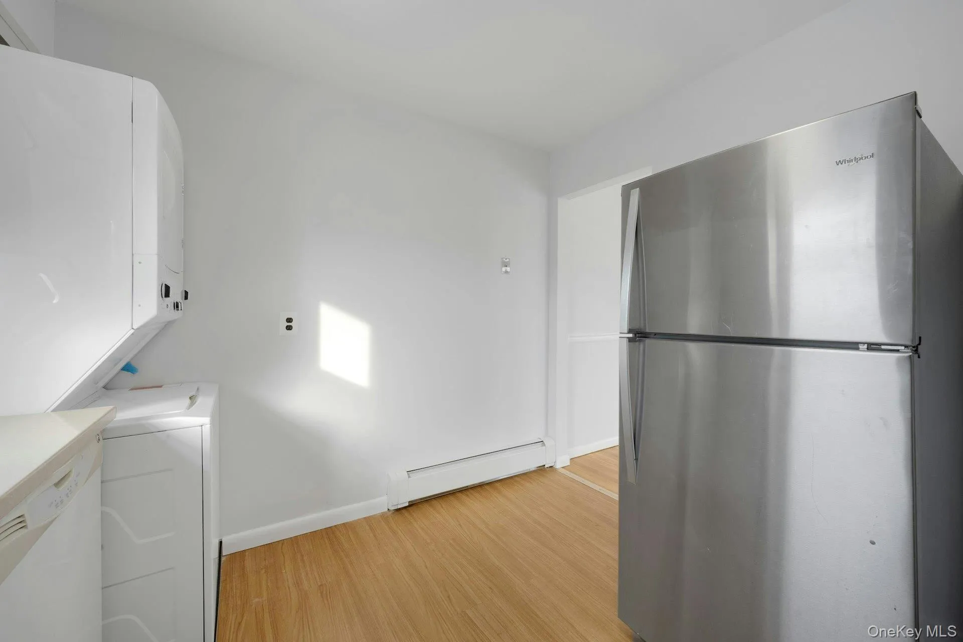 Kitchen with freestanding refrigerator, white cabinetry, baseboard heating, light wood-style flooring, and light countertops Kitchen with freestanding refrigerator, white cabinetry, baseboard heating, light wood-style flooring, and light countertops