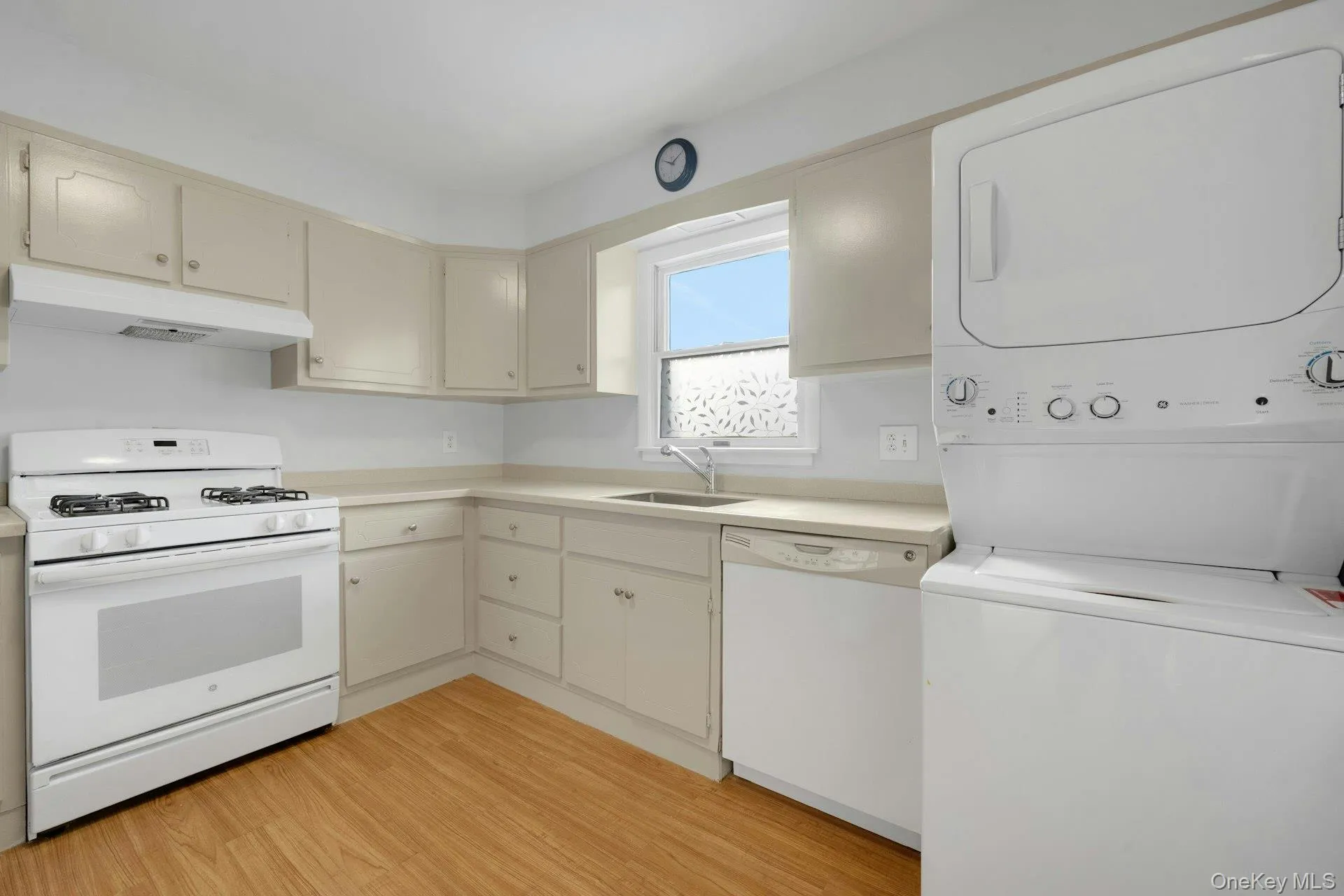 Kitchen with white appliances, light countertops, under cabinet range hood, light wood-style flooring, and stacked washing machine and dryer Kitchen with white appliances, light countertops, under cabinet range hood, light wood-style flooring, and stacked washing machine and dryer