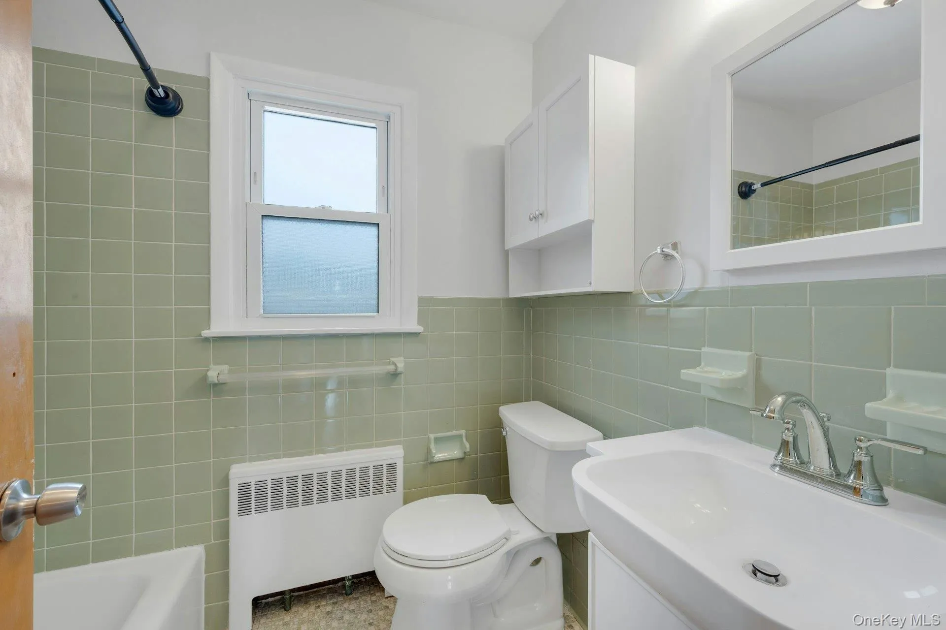 Bathroom with radiator heating unit, vanity, a wainscoted wall, tile walls, and shower / tub combination Bathroom with radiator heating unit, vanity, a wainscoted wall, tile walls, and shower / tub combination