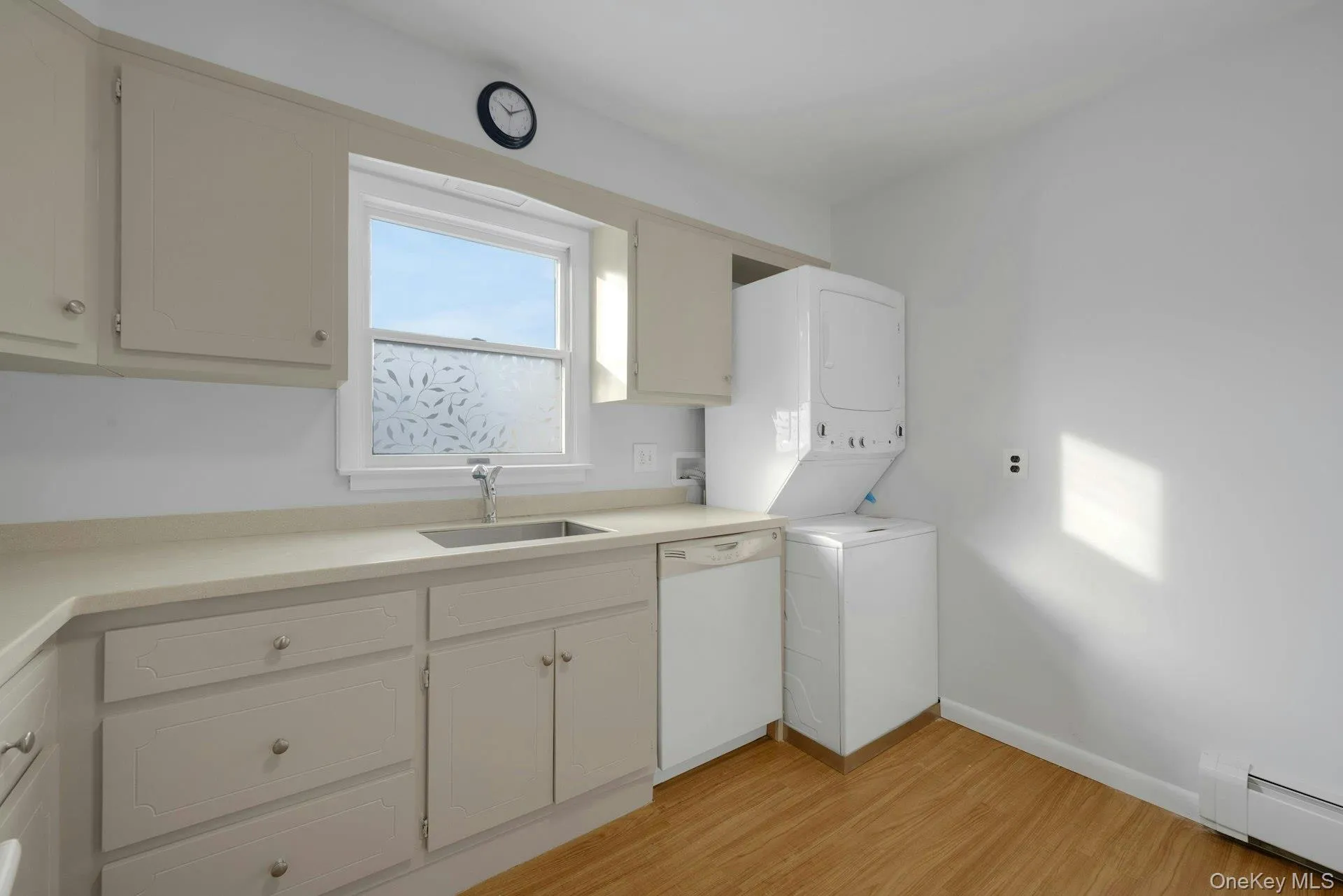 Laundry room with baseboard heating, stacked washing machine and dryer, and light wood-type flooring Laundry room with baseboard heating, stacked washing machine and dryer, and light wood-type flooring
