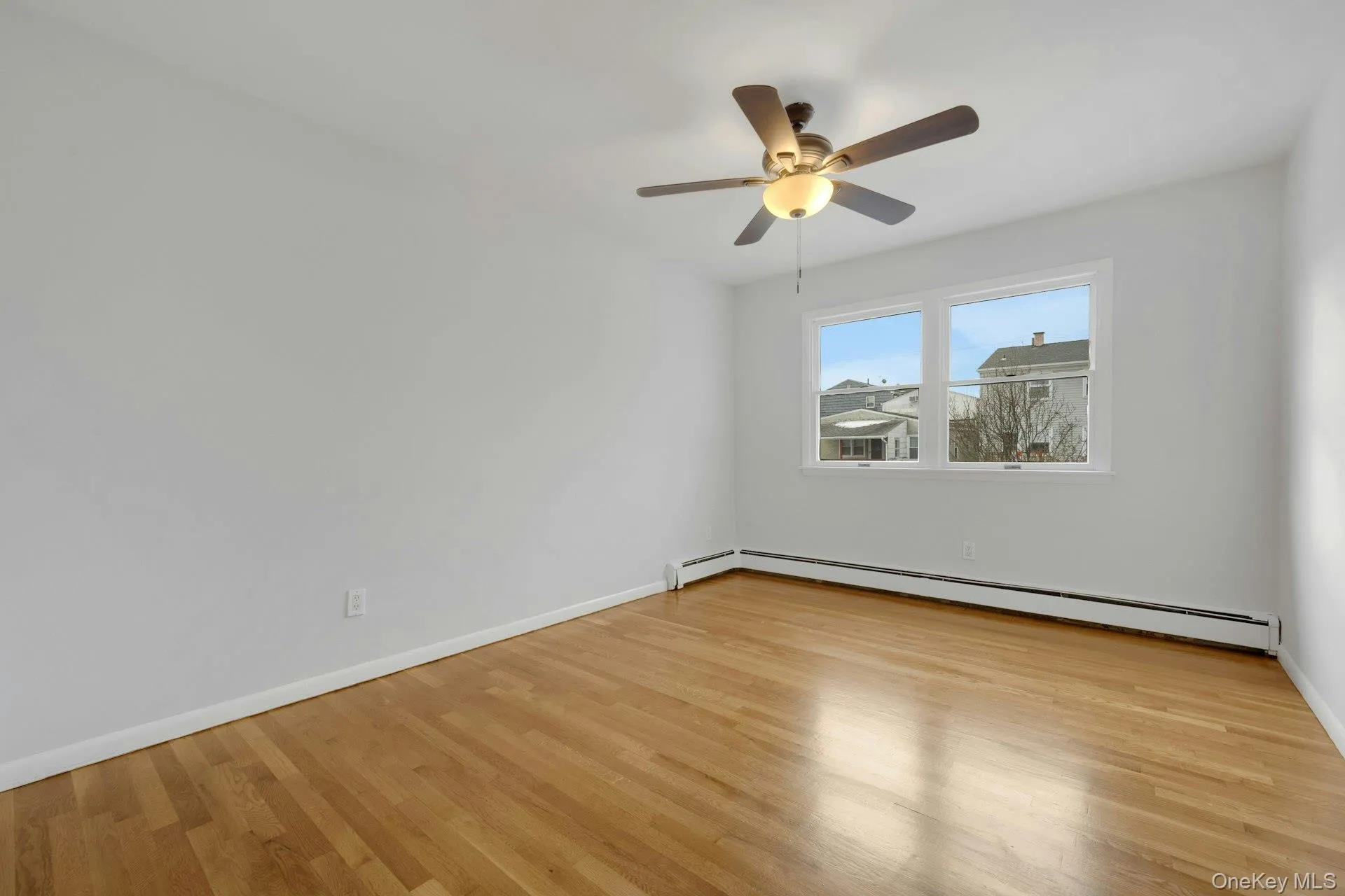 Empty room with light wood-style floors, baseboard heating, and a ceiling fan Empty room with light wood-style floors, baseboard heating, and a ceiling fan