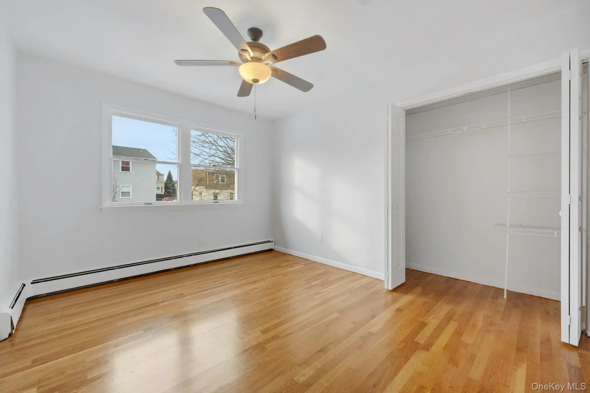 Unfurnished bedroom with light wood finished floors, ceiling fan, a closet, and a baseboard radiator Unfurnished bedroom with light wood finished floors, ceiling fan, a closet, and a baseboard radiator