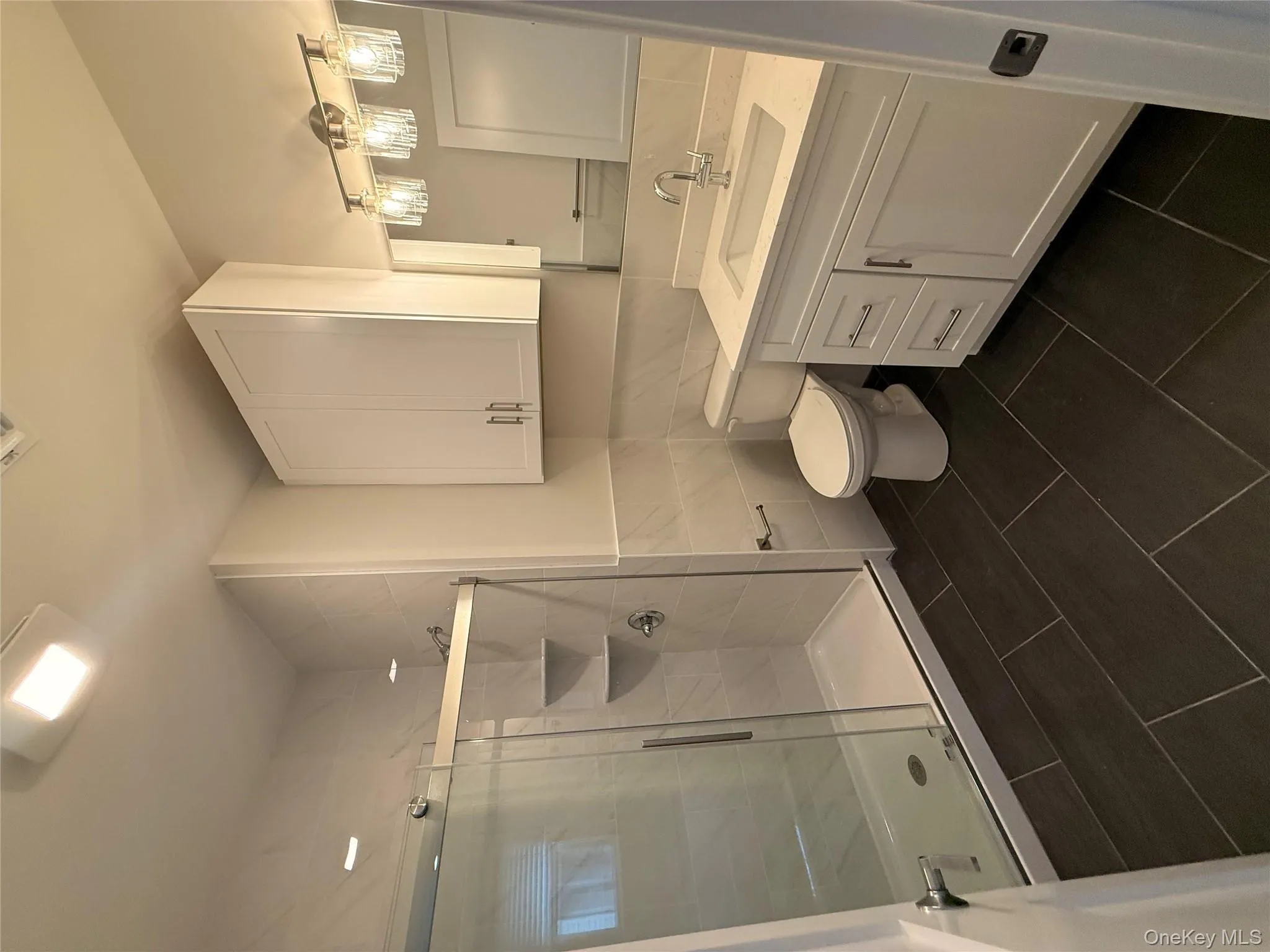Full bathroom featuring a shower stall, tile walls, vanity, dark tile patterned flooring, and a wainscoted wall Full bathroom featuring a shower stall, tile walls, vanity, dark tile patterned flooring, and a wainscoted wall