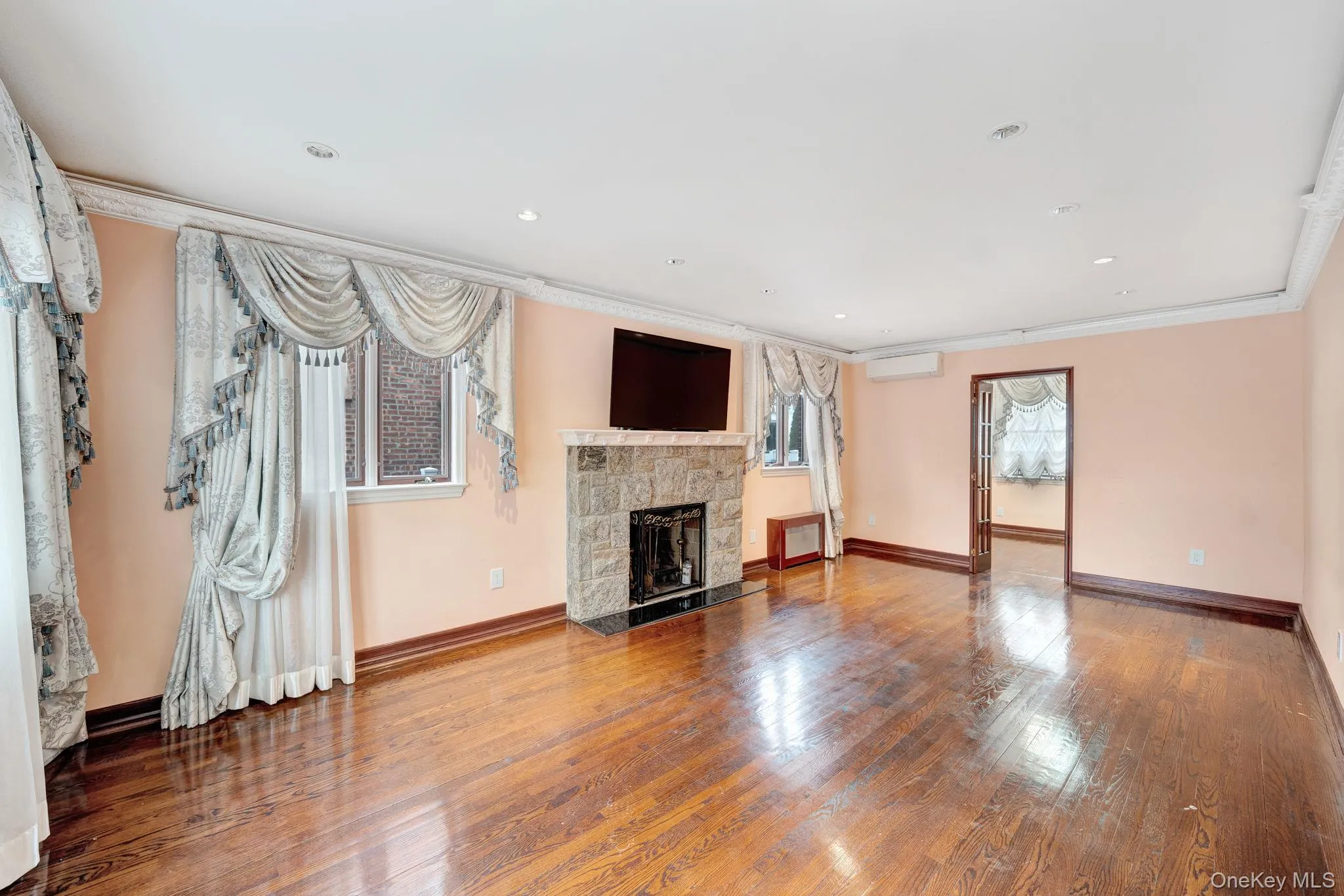 Unfurnished living room featuring a stone fireplace, hardwood / wood-style flooring, recessed lighting, ornamental molding, and an AC wall unit Unfurnished living room featuring a stone fireplace, hardwood / wood-style flooring, recessed lighting, ornamental molding, and an AC wall unit
