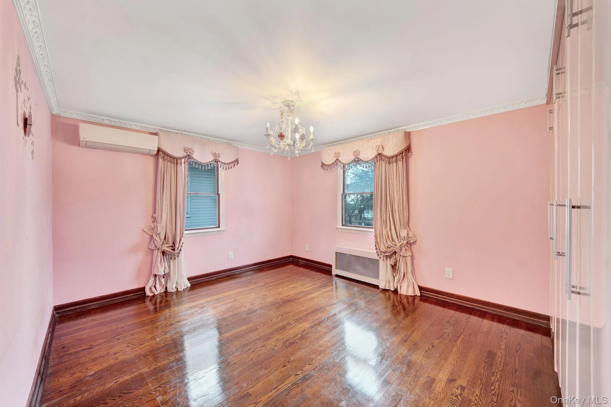 Empty room with hardwood / wood-style floors, a chandelier, radiator, and a wall mounted air conditioner Empty room with hardwood / wood-style floors, a chandelier, radiator, and a wall mounted air conditioner