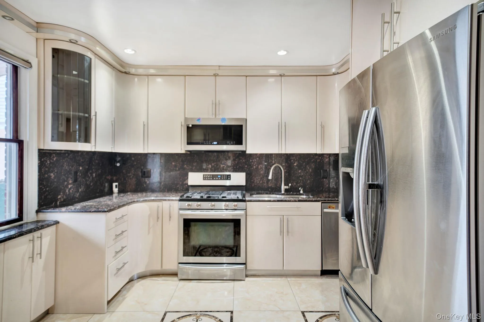 Kitchen with stainless steel appliances, dark stone countertops, light tile patterned flooring, glass insert cabinets, and tasteful backsplash Kitchen with stainless steel appliances, dark stone countertops, light tile patterned flooring, glass insert cabinets, and tasteful backsplash