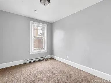Carpeted empty room with baseboards and a baseboard radiator Carpeted empty room with baseboards and a baseboard radiator