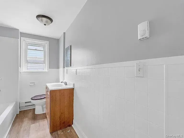 Full bathroom featuring vanity, light wood-type flooring, a baseboard radiator, wainscoting, and tub / shower combination Full bathroom featuring vanity, light wood-type flooring, a baseboard radiator, wainscoting, and tub / shower combination