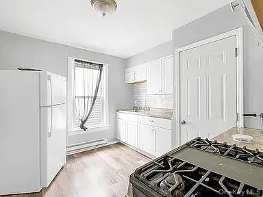Kitchen featuring freestanding refrigerator, white cabinetry, light countertops, backsplash, and light wood finished floors Kitchen featuring freestanding refrigerator, white cabinetry, light countertops, backsplash, and light wood finished floors