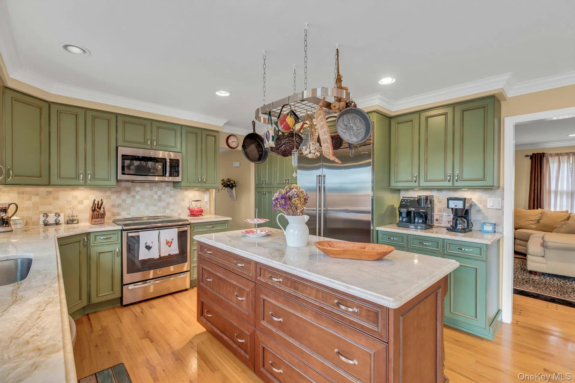 Kitchen with green cabinetry, crown molding, stainless steel appliances, light stone countertops, and a kitchen island