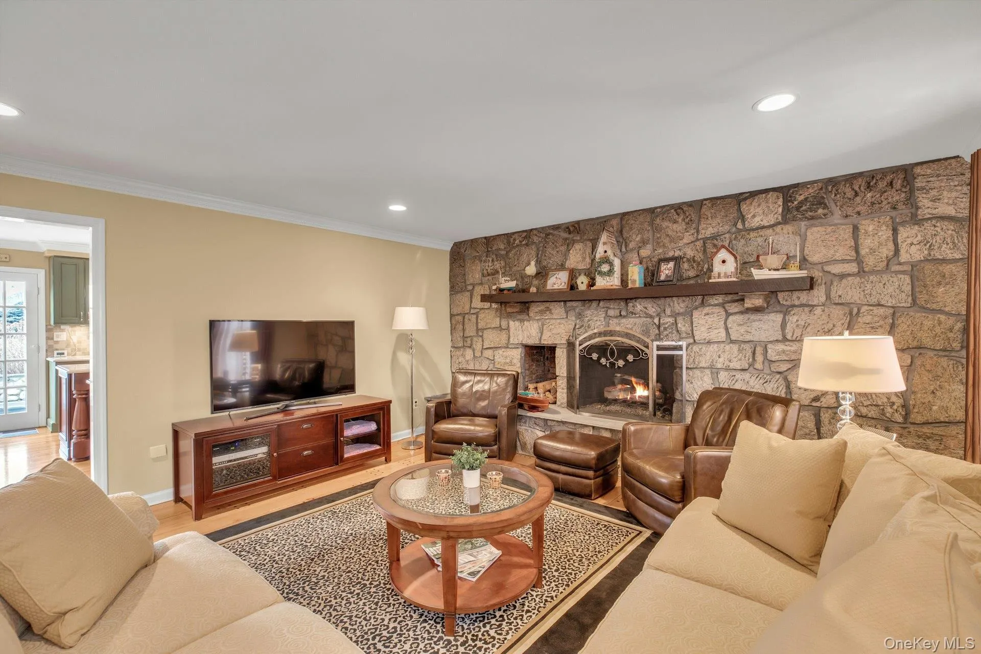 Living area with wood finished floors, a stone fireplace, recessed lighting, and crown molding
