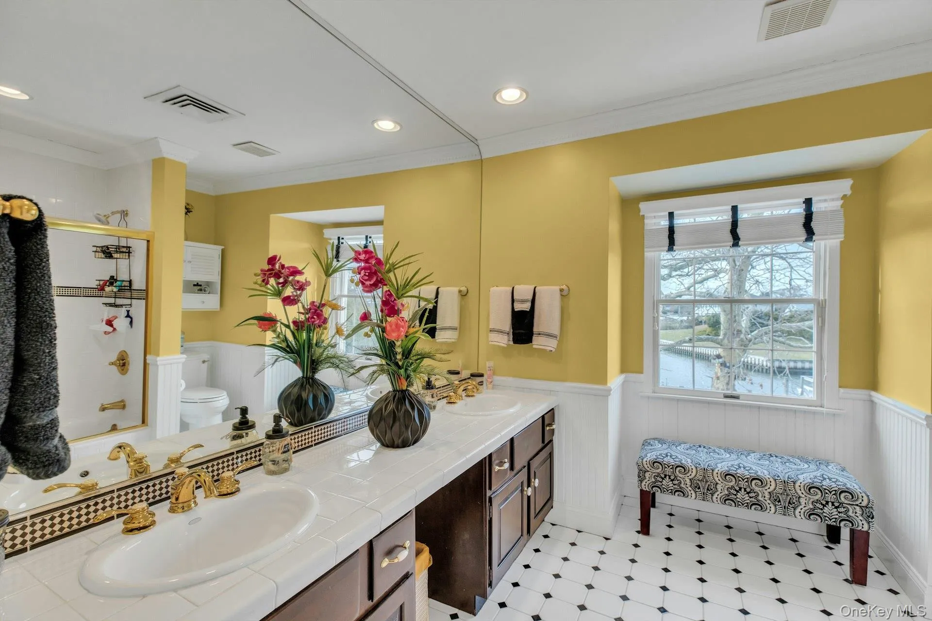 Full bathroom featuring a wainscoted wall, double vanity, crown molding, healthy amount of natural light, and bath / shower combo with glass door