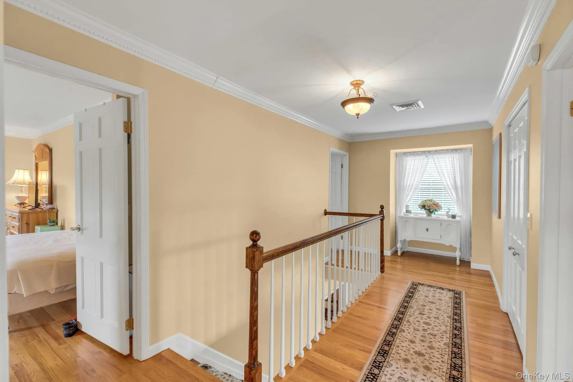 Hall with ornamental molding, light wood-style flooring, and an upstairs landing