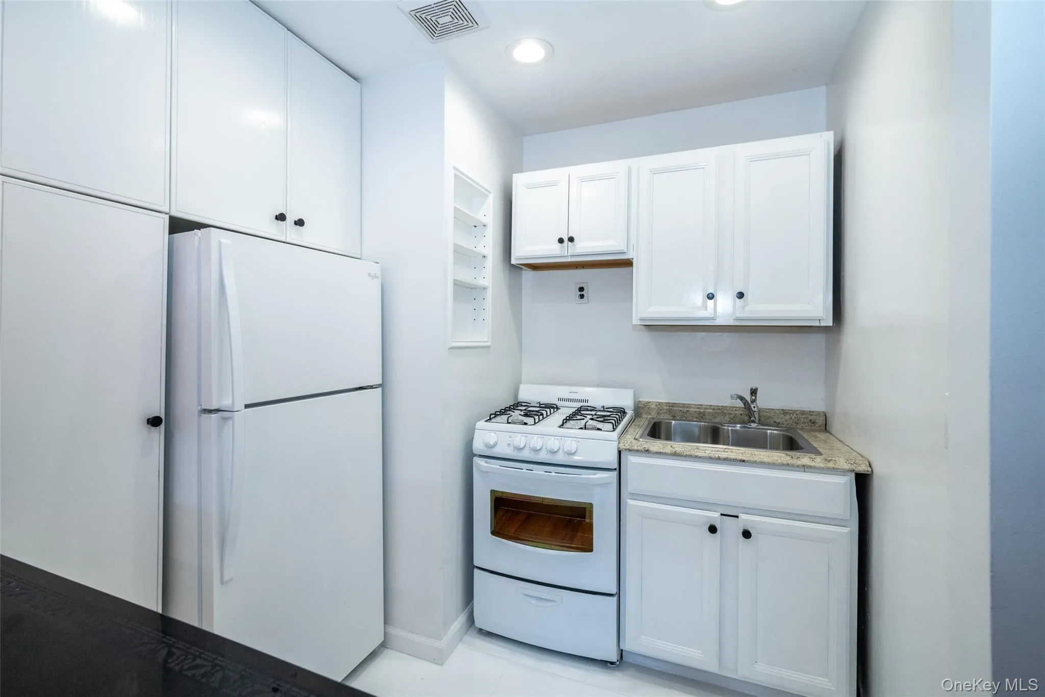 Kitchen with white appliances, white cabinetry, recessed lighting, and light stone countertops Kitchen with white appliances, white cabinetry, recessed lighting, and light stone countertops