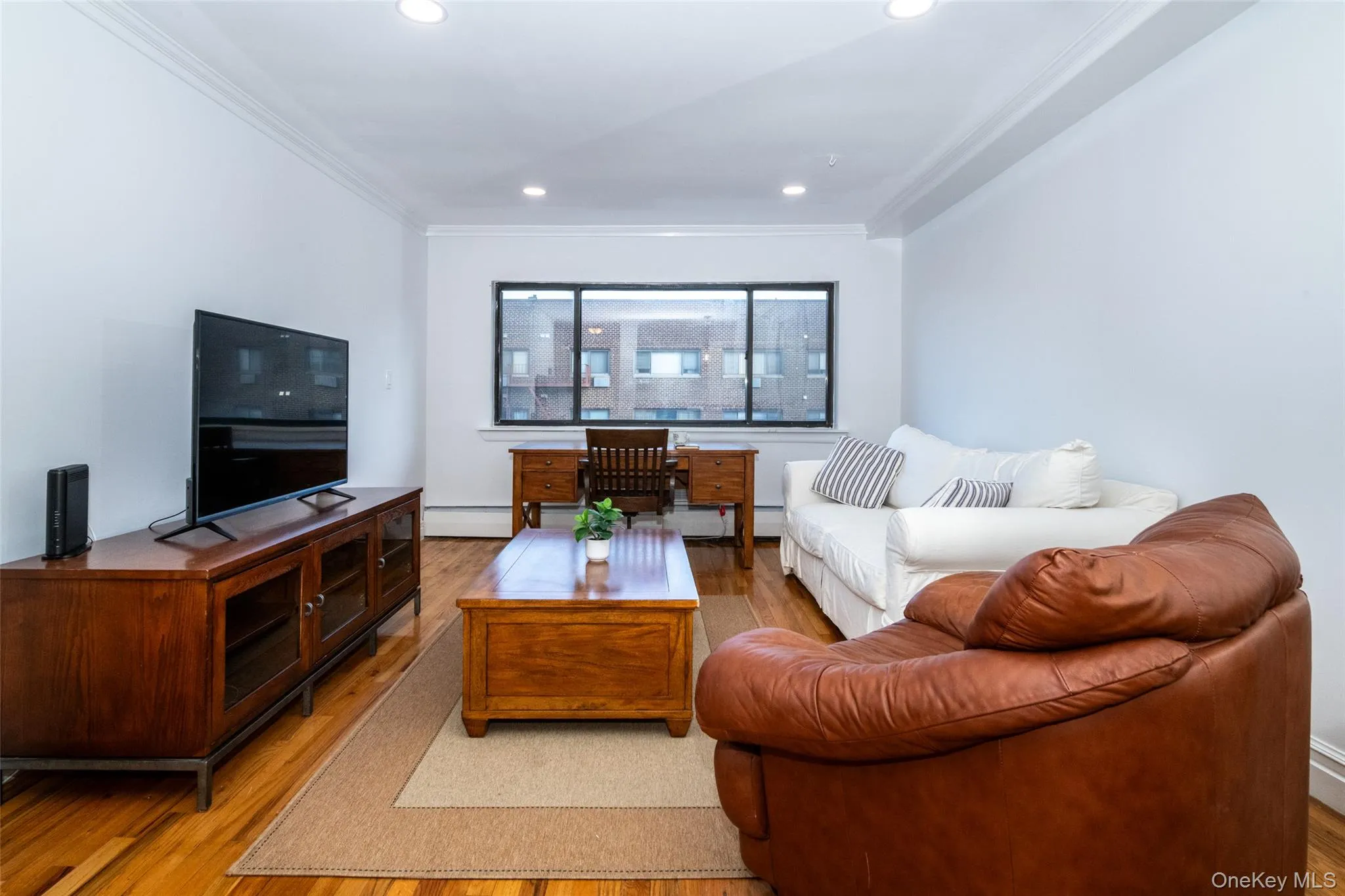 Living area with recessed lighting, wood finished floors, crown molding, and a baseboard heating unit Living area with recessed lighting, wood finished floors, crown molding, and a baseboard heating unit