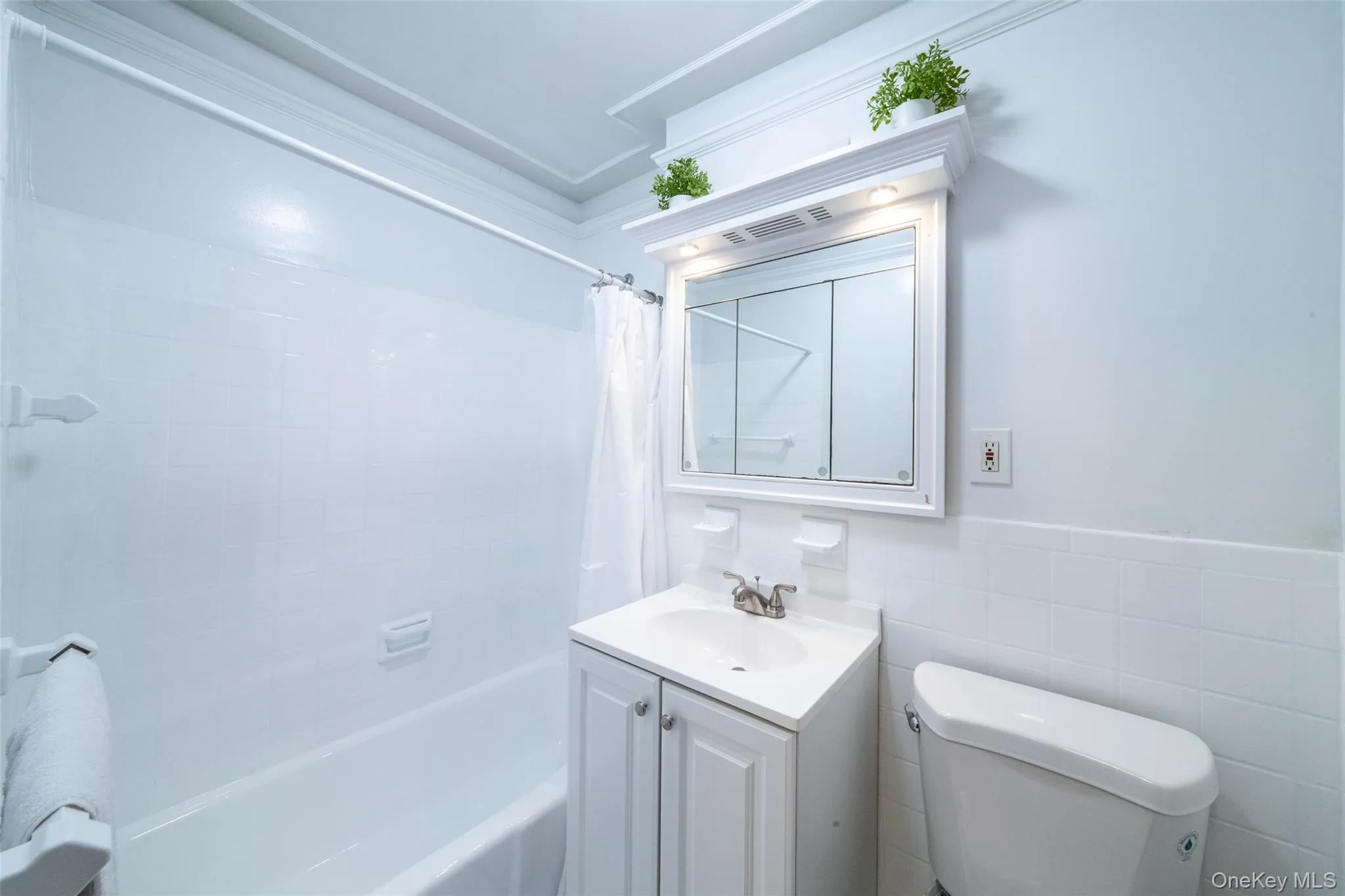 Bathroom with shower / bath combo with shower curtain, tile walls, a wainscoted wall, and vanity Bathroom with shower / bath combo with shower curtain, tile walls, a wainscoted wall, and vanity