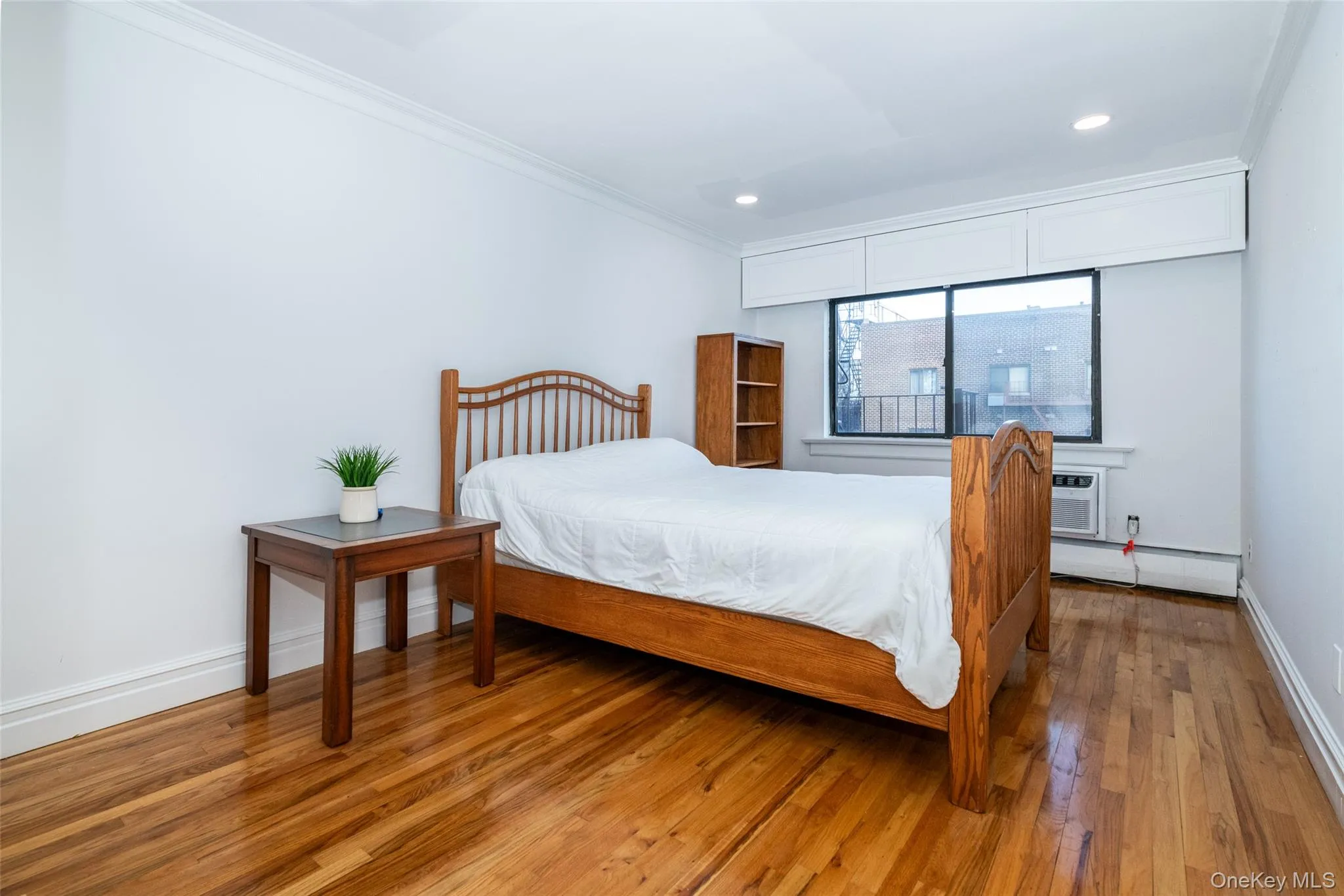 Bedroom with light wood-style flooring, a baseboard heating unit, recessed lighting, a wall mounted AC, and crown molding Bedroom with light wood-style flooring, a baseboard heating unit, recessed lighting, a wall mounted AC, and crown molding
