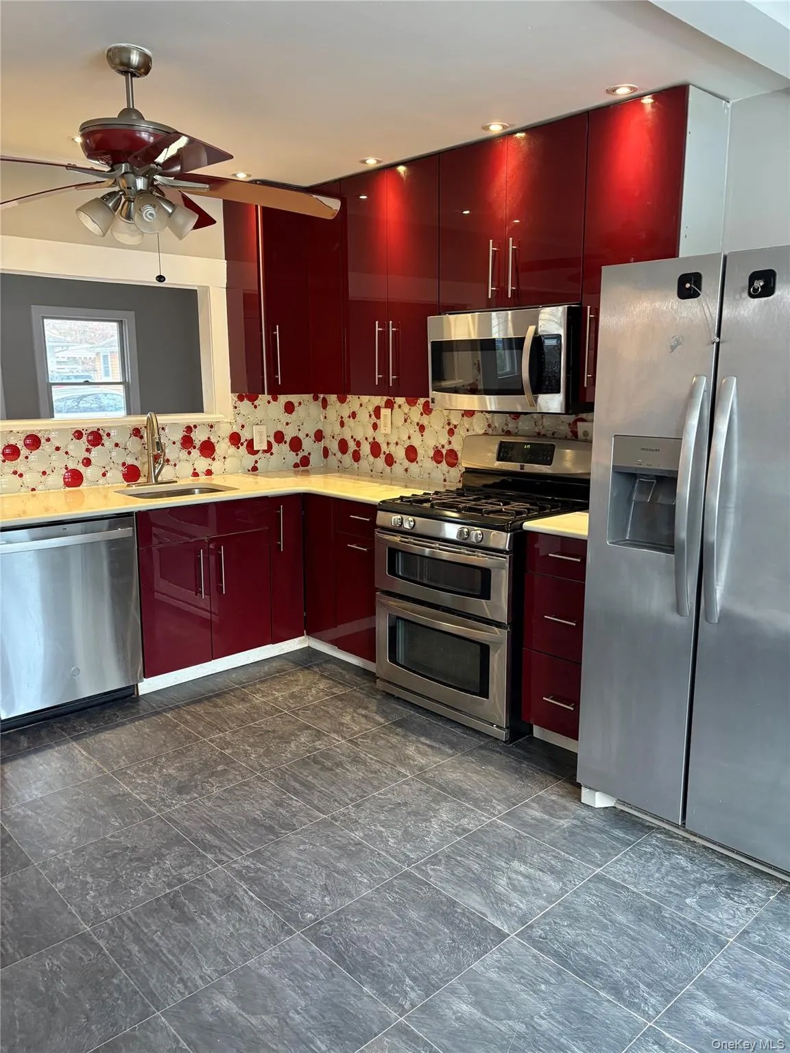 Kitchen with appliances with stainless steel finishes, red cabinets, backsplash, and a ceiling fan Kitchen with appliances with stainless steel finishes, red cabinets, backsplash, and a ceiling fan