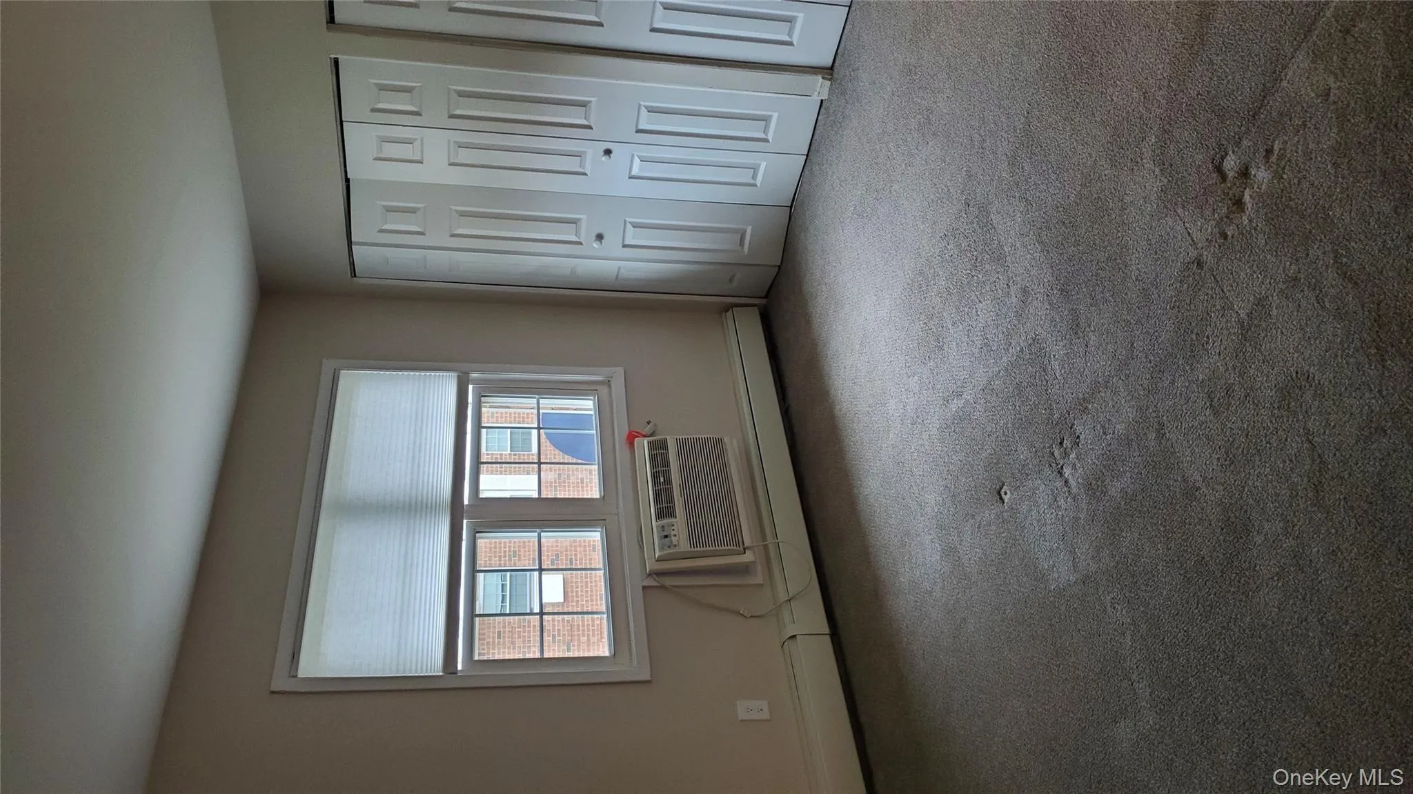 Unfurnished bedroom with baseboard heating, a closet, carpet flooring, and an AC wall unit Unfurnished bedroom with baseboard heating, a closet, carpet flooring, and an AC wall unit