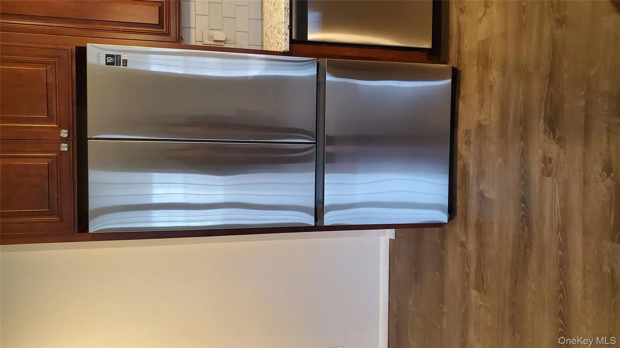 Kitchen view of freestanding refrigerator, light stone countertops, dishwasher, dark wood-type flooring, and brown cabinets Kitchen view of freestanding refrigerator, light stone countertops, dishwasher, dark wood-type flooring, and brown cabinets