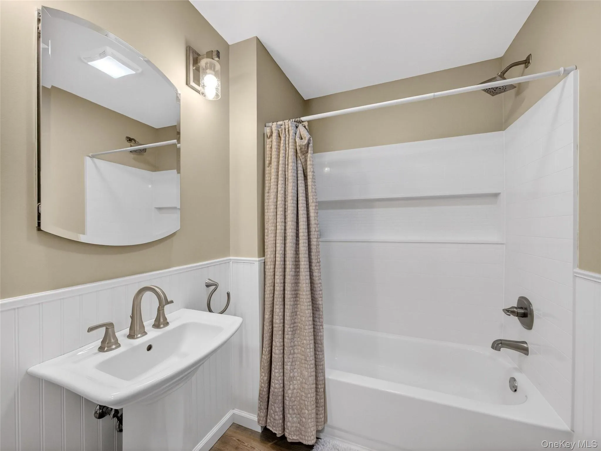 Bathroom featuring a wainscoted wall, shower / bath combo, and wood finished floors Bathroom featuring a wainscoted wall, shower / bath combo, and wood finished floors