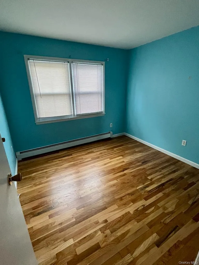Spare room featuring wood finished floors and a baseboard heating unit Spare room featuring wood finished floors and a baseboard heating unit