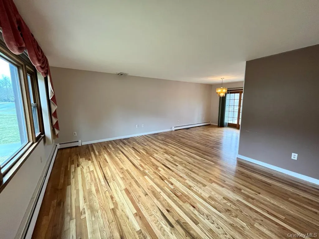 Unfurnished room featuring a chandelier, baseboard heating, light wood-style flooring, and a baseboard radiator Unfurnished room featuring a chandelier, baseboard heating, light wood-style flooring, and a baseboard radiator