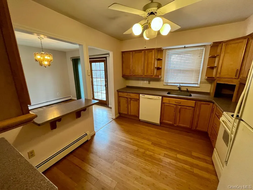 Kitchen with open shelves, brown cabinetry, baseboard heating, and dark countertops Kitchen with open shelves, brown cabinetry, baseboard heating, and dark countertops
