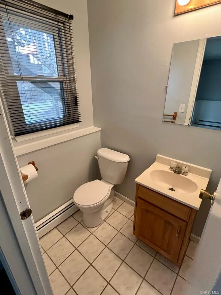 Half bath featuring vanity, a baseboard radiator, and light tile patterned floors Half bath featuring vanity, a baseboard radiator, and light tile patterned floors