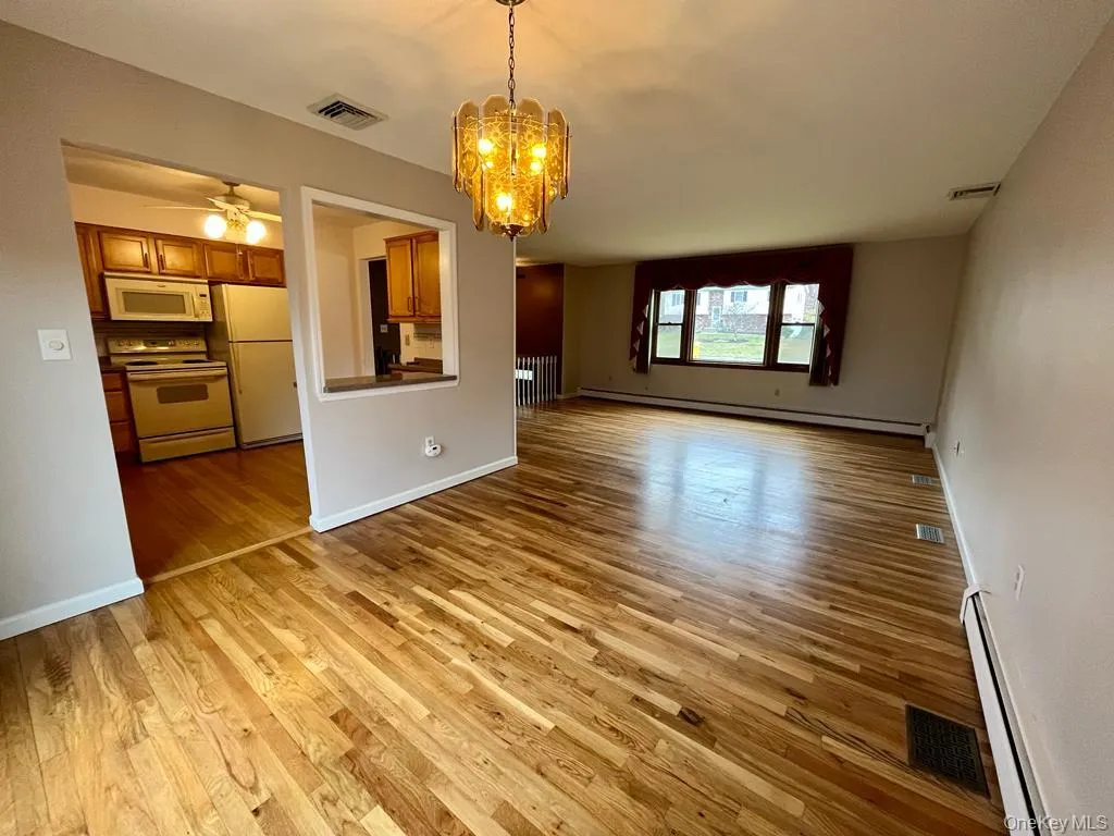 Unfurnished living room with baseboard heating, a chandelier, light wood finished floors, and ceiling fan Unfurnished living room with baseboard heating, a chandelier, light wood finished floors, and ceiling fan