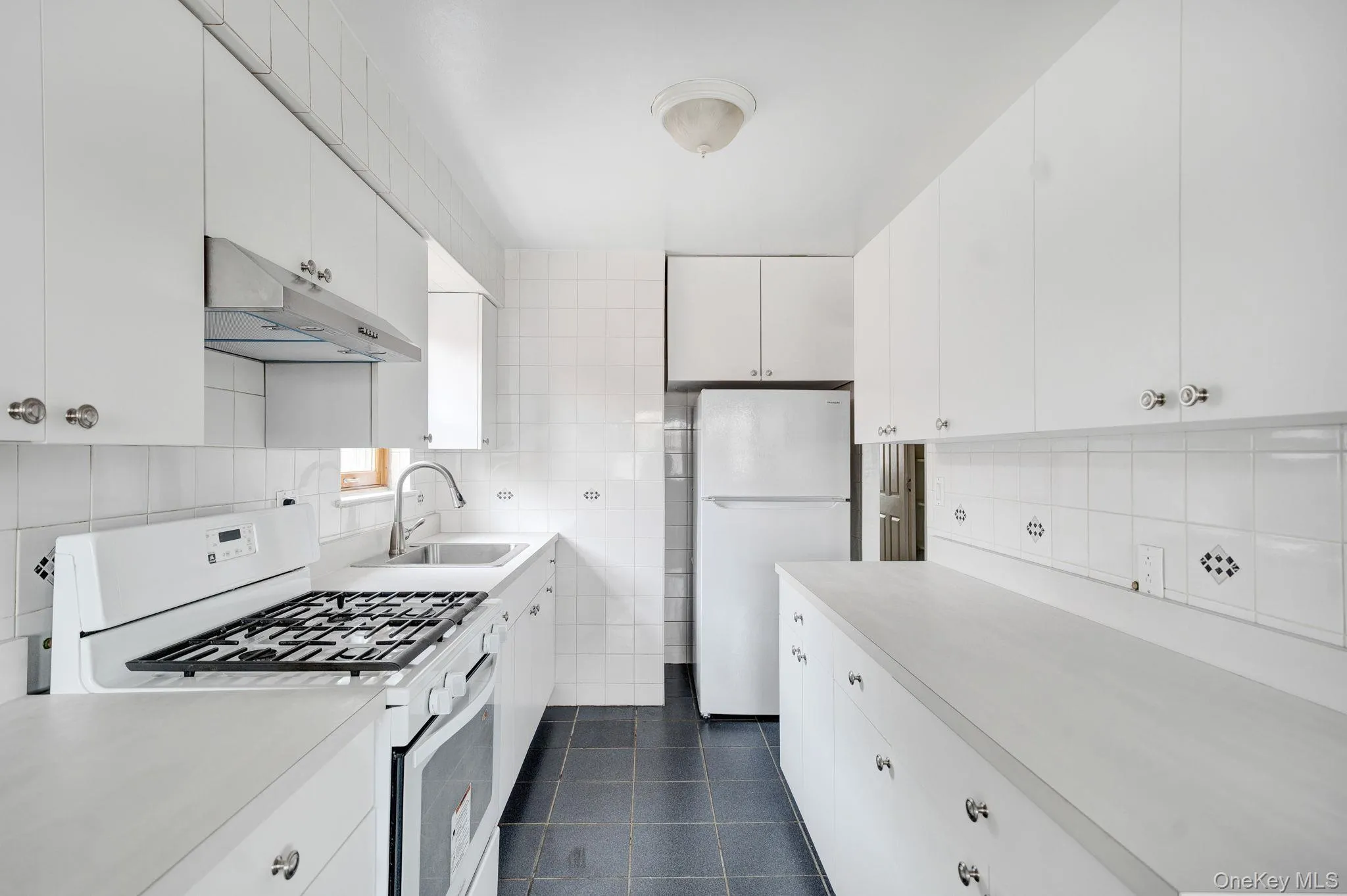 Kitchen featuring white appliances, light countertops, under cabinet range hood, white cabinetry, and tasteful backsplash Kitchen featuring white appliances, light countertops, under cabinet range hood, white cabinetry, and tasteful backsplash