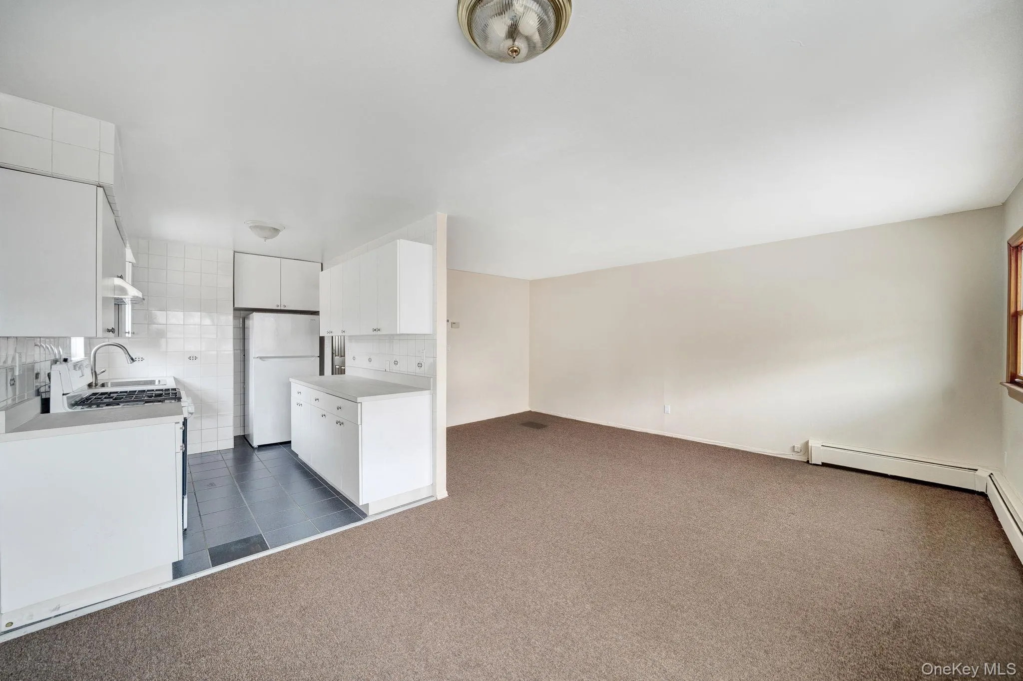 Kitchen with dark colored carpet, light countertops, decorative backsplash, freestanding refrigerator, and range with gas stovetop Kitchen with dark colored carpet, light countertops, decorative backsplash, freestanding refrigerator, and range with gas stovetop