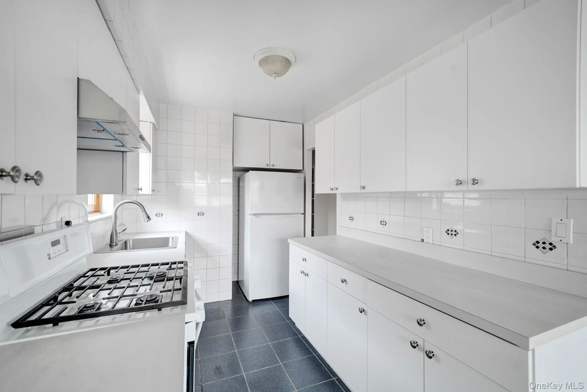 Kitchen with gas stove, decorative backsplash, light countertops, freestanding refrigerator, and tile walls Kitchen with gas stove, decorative backsplash, light countertops, freestanding refrigerator, and tile walls